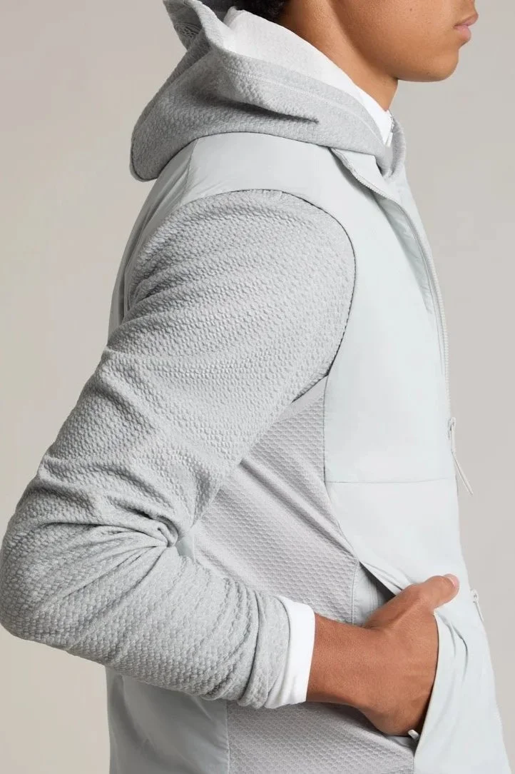 Side view of a person wearing a gray hoodie and white textured jacket, with the person's hand in their pocket.