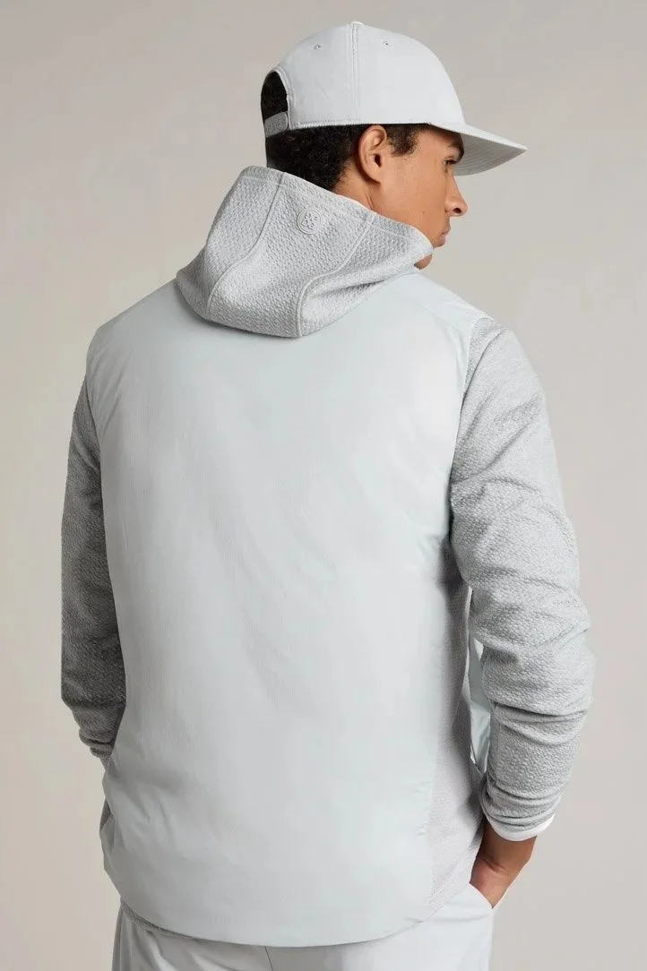 Rear view of a young man wearing a white baseball cap, white jacket with gray sleeves, and standing against a plain background.