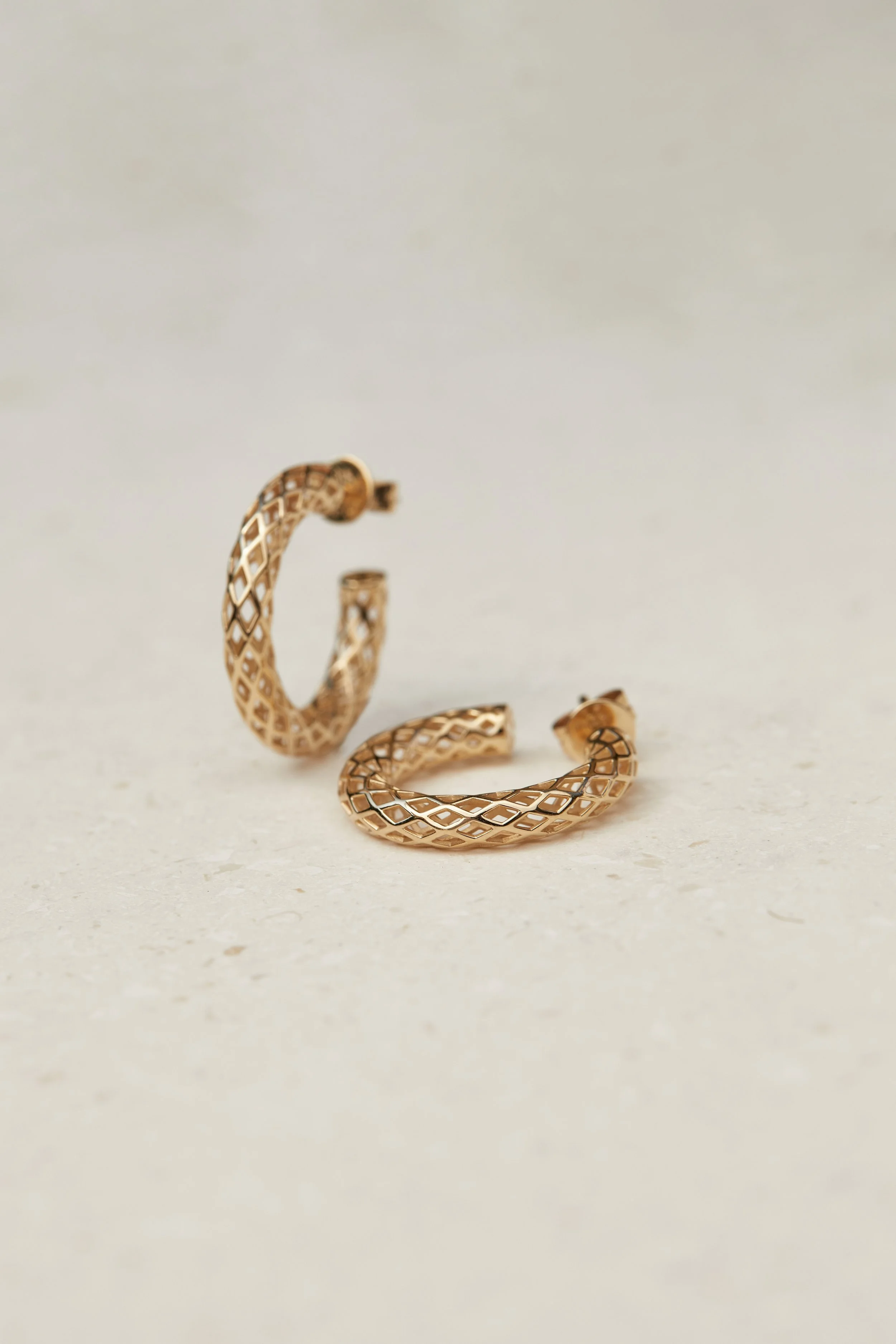 A pair of gold textured hoop earrings placed on a light-colored surface.
