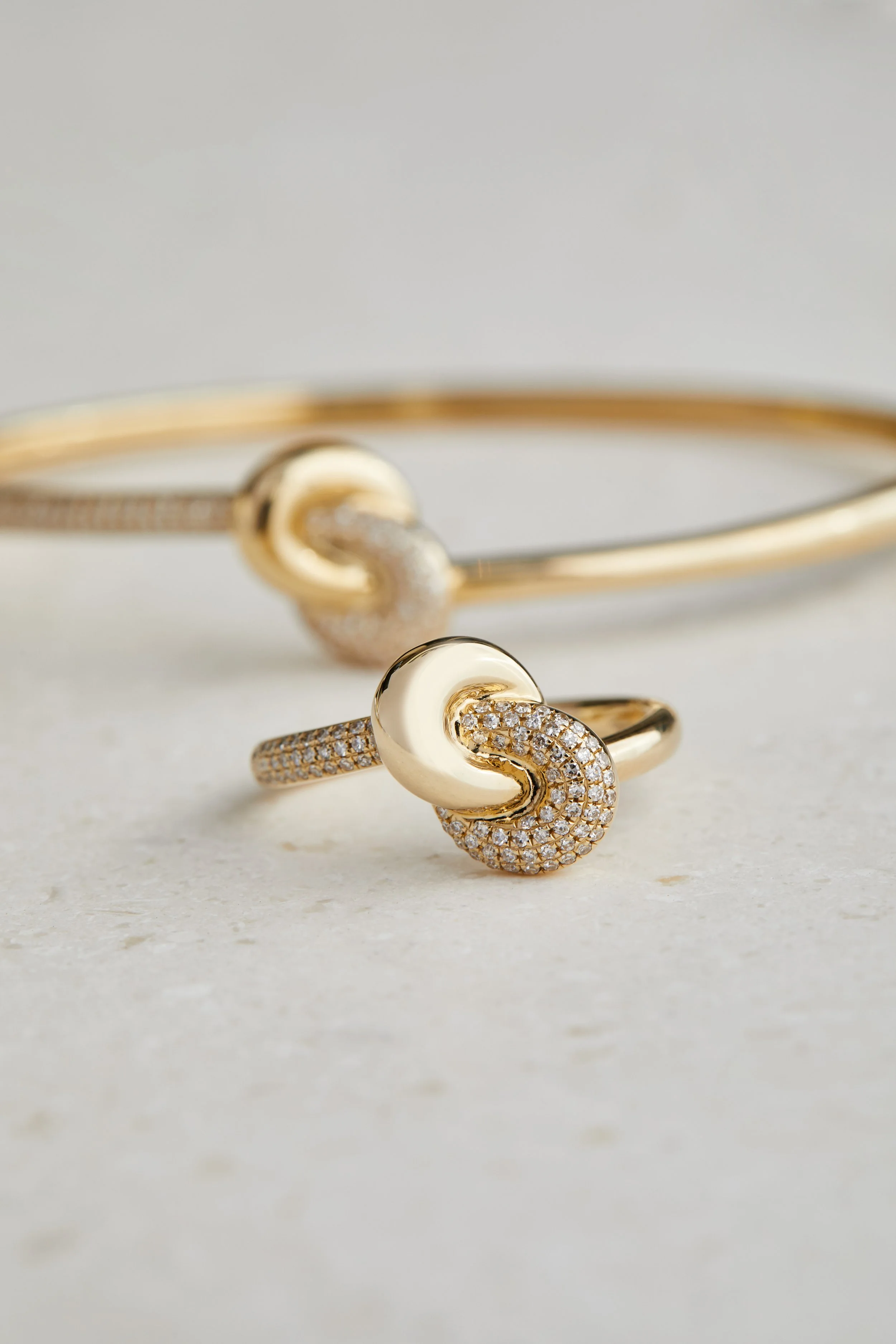Close-up of a gold and diamond jewelry set, including a bracelet and a ring, with the ring prominently in focus and the bracelet slightly blurred in the background.