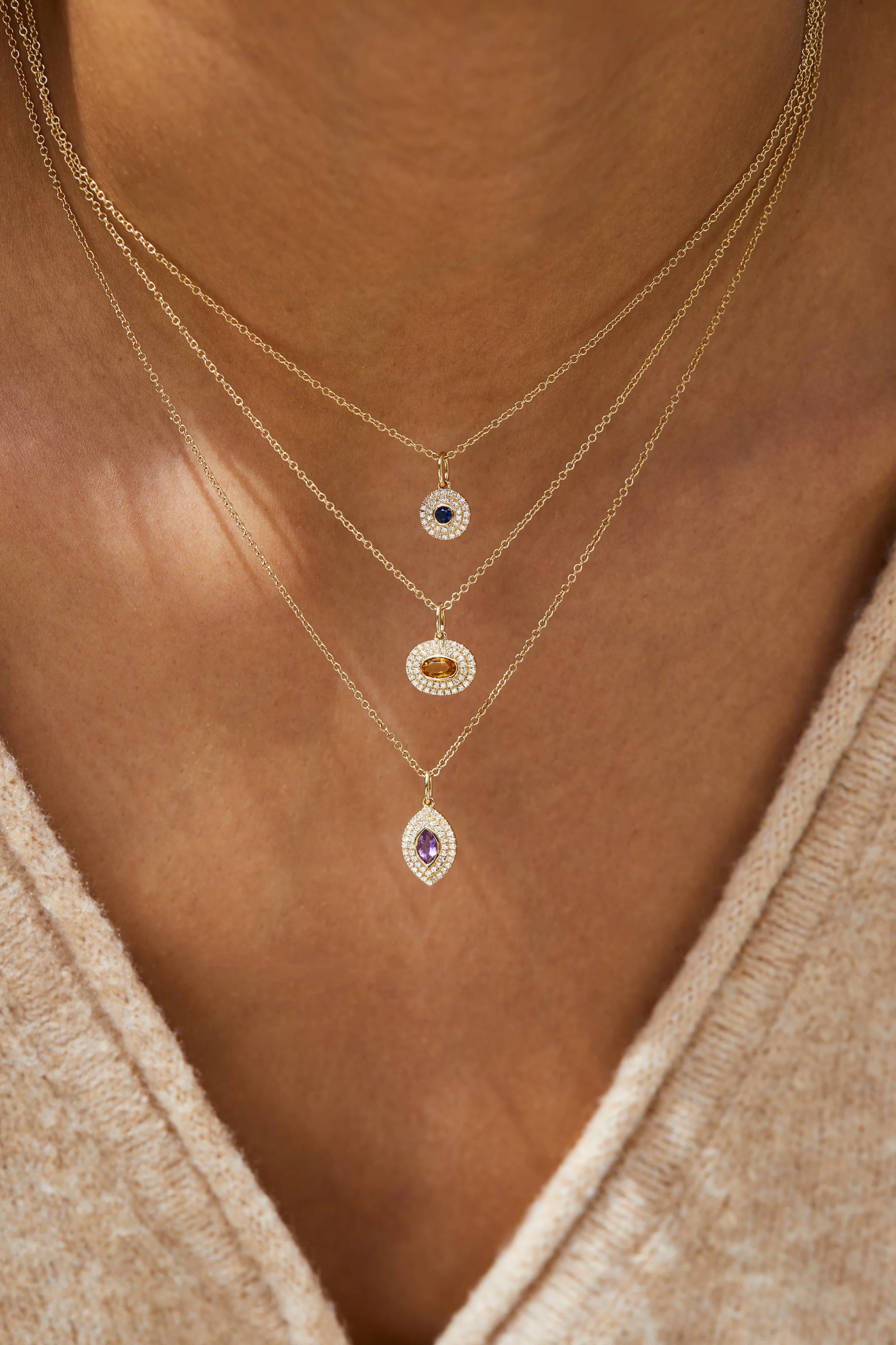 Close-up photo of a woman wearing three layered gold necklaces with pendant charms decorated with colored stones and small diamonds.