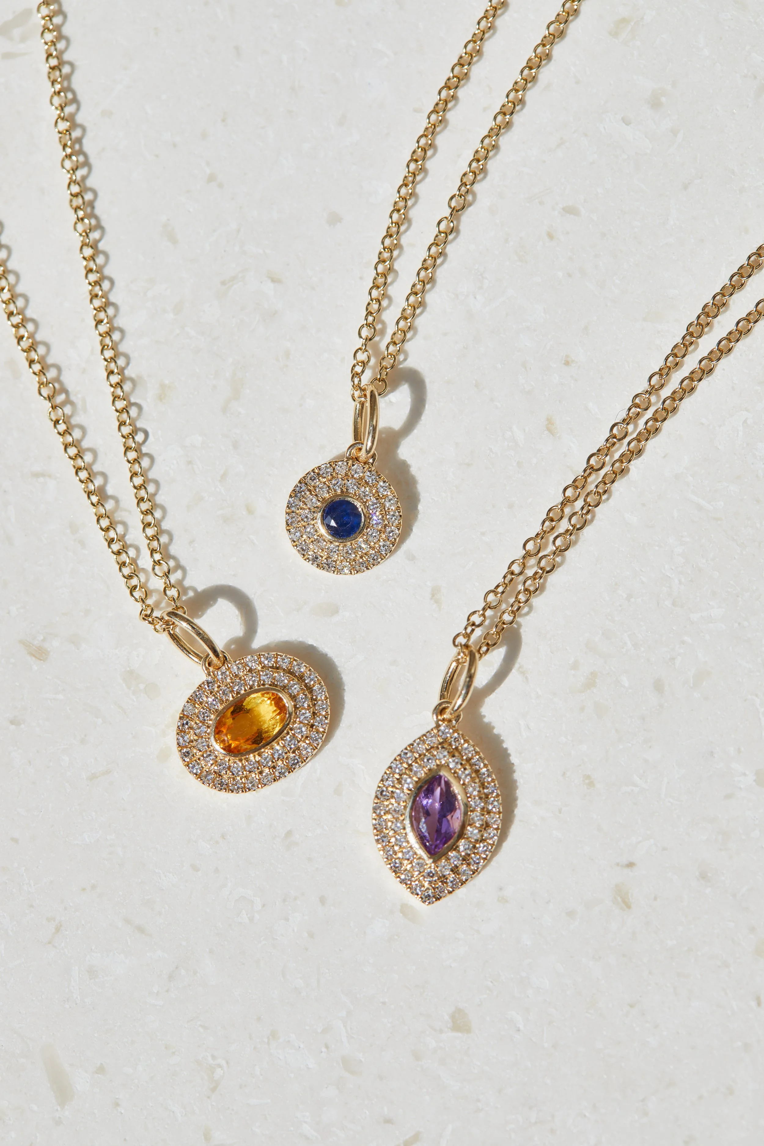 Three gold chains with colorful gemstone pendant necklaces, each surrounded by small diamonds.