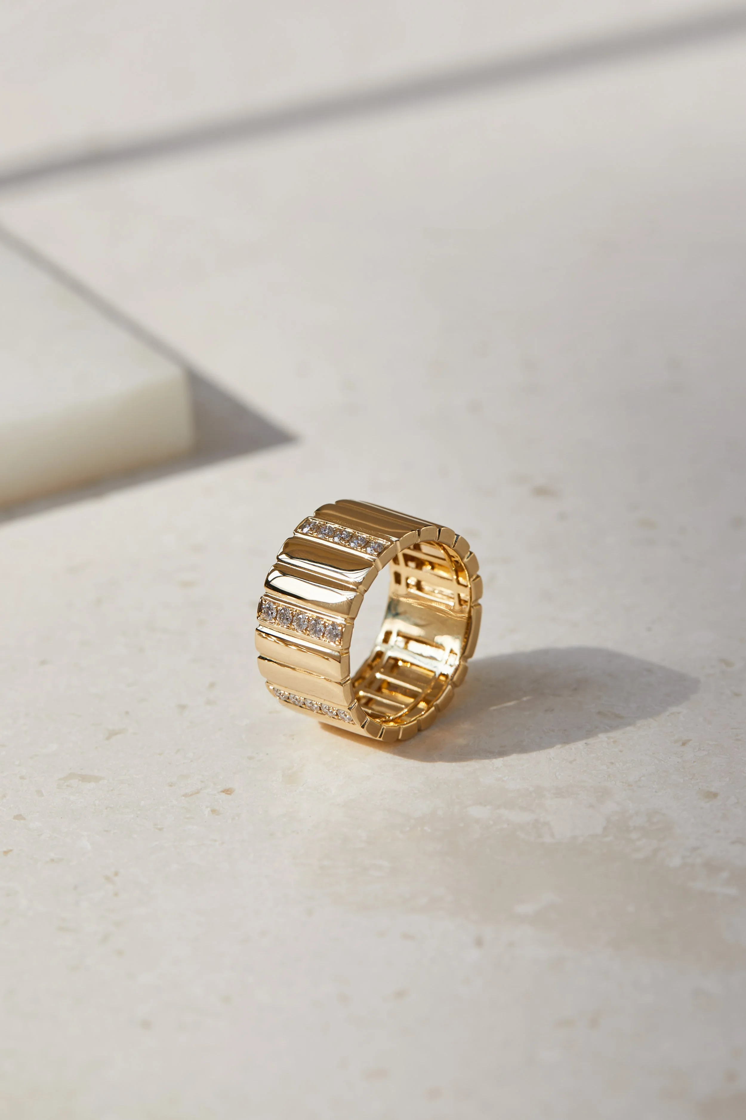 Gold ring with embedded diamonds on a white surface with a shadow.