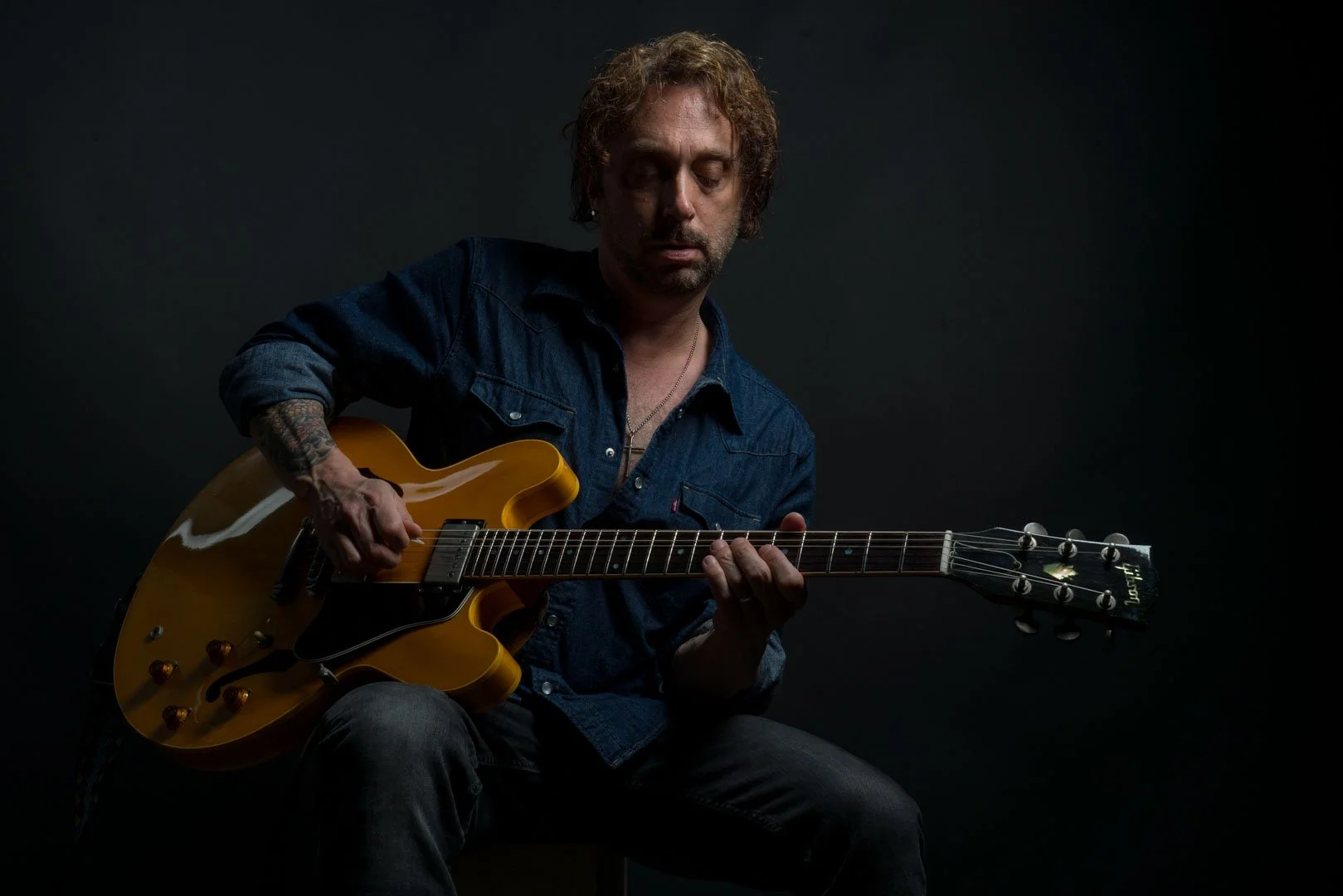 Headshot of a man wearing a blue shirt and jeans and playing an electric guitar