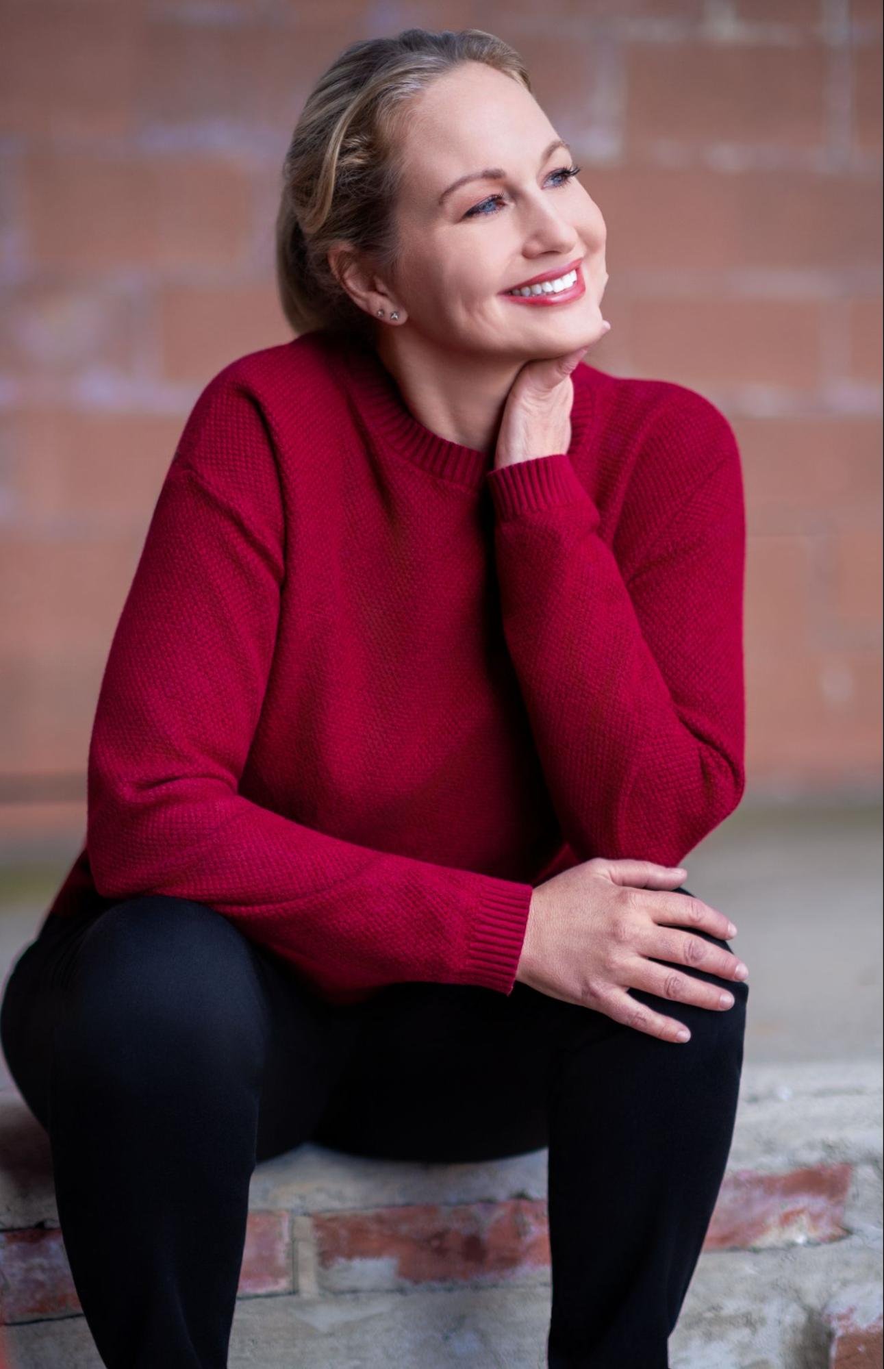 Headshot of a woman with blond hair pulled into a pony tail wearing a red shirt and smiling to the side