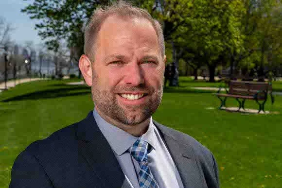 Headshot of a man in a park wearing a blue suit and smiling.