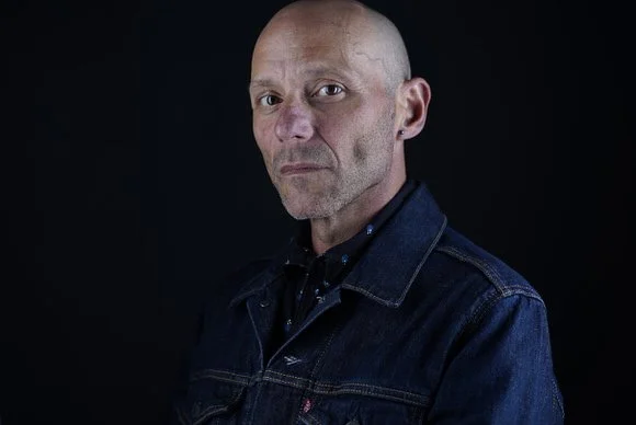 Headshot of a bald man wearing a blue denim jacket who is a professional actor