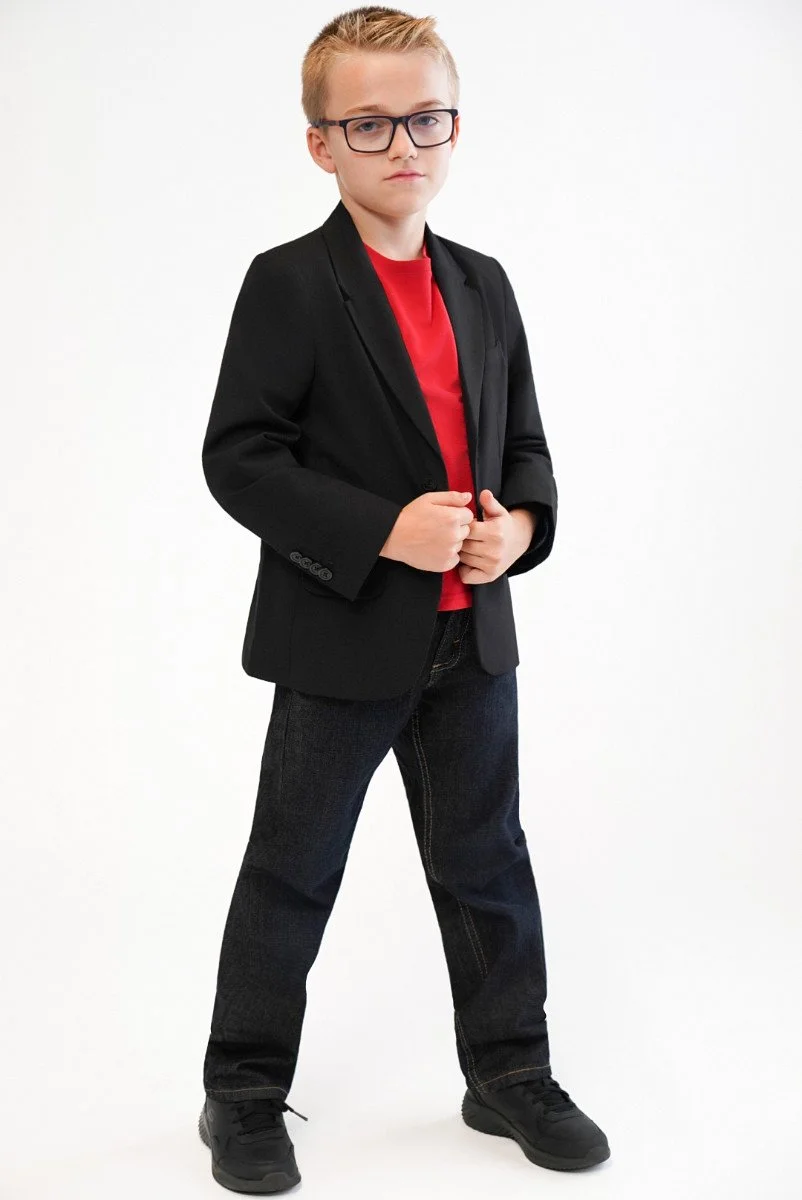 A young boy with blonde hair and glasses wearing a black blazer with a red undershirt