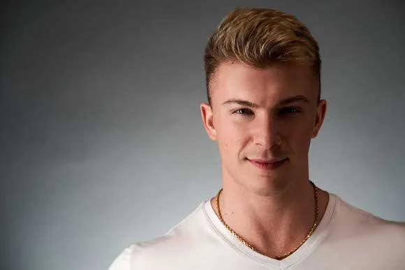 Headshot of a young blonde man in a white V-neck t-shirt.