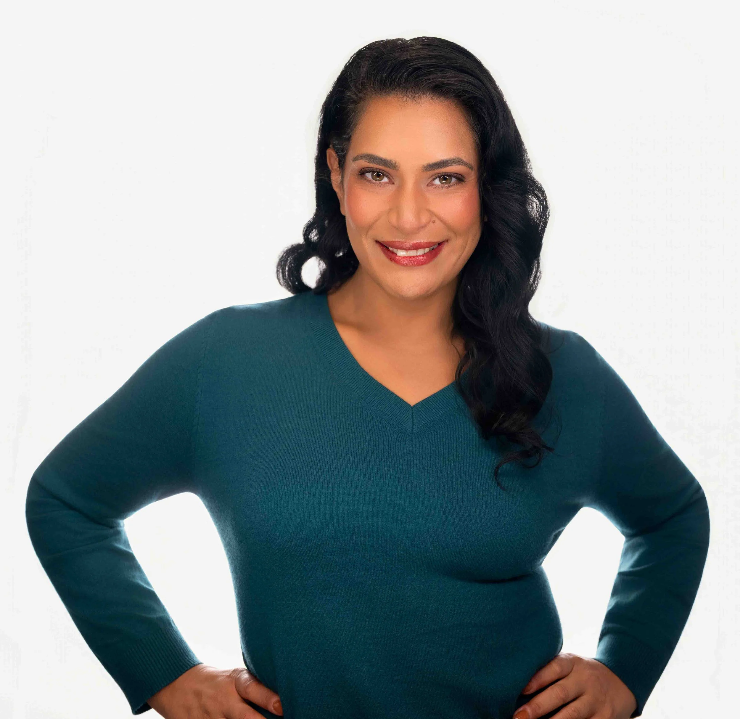 A hispanic woman with a teal sweater posing with her hands on her hips and smiling.