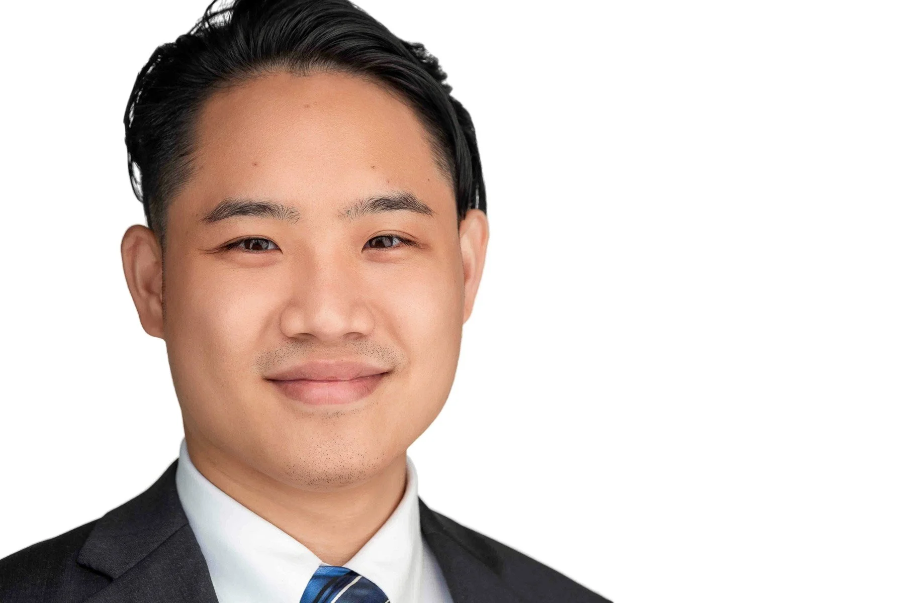 Portrait of a young man with short black hair, wearing a black suit, white shirt, and a blue-striped tie, smiling at the camera against a white background.