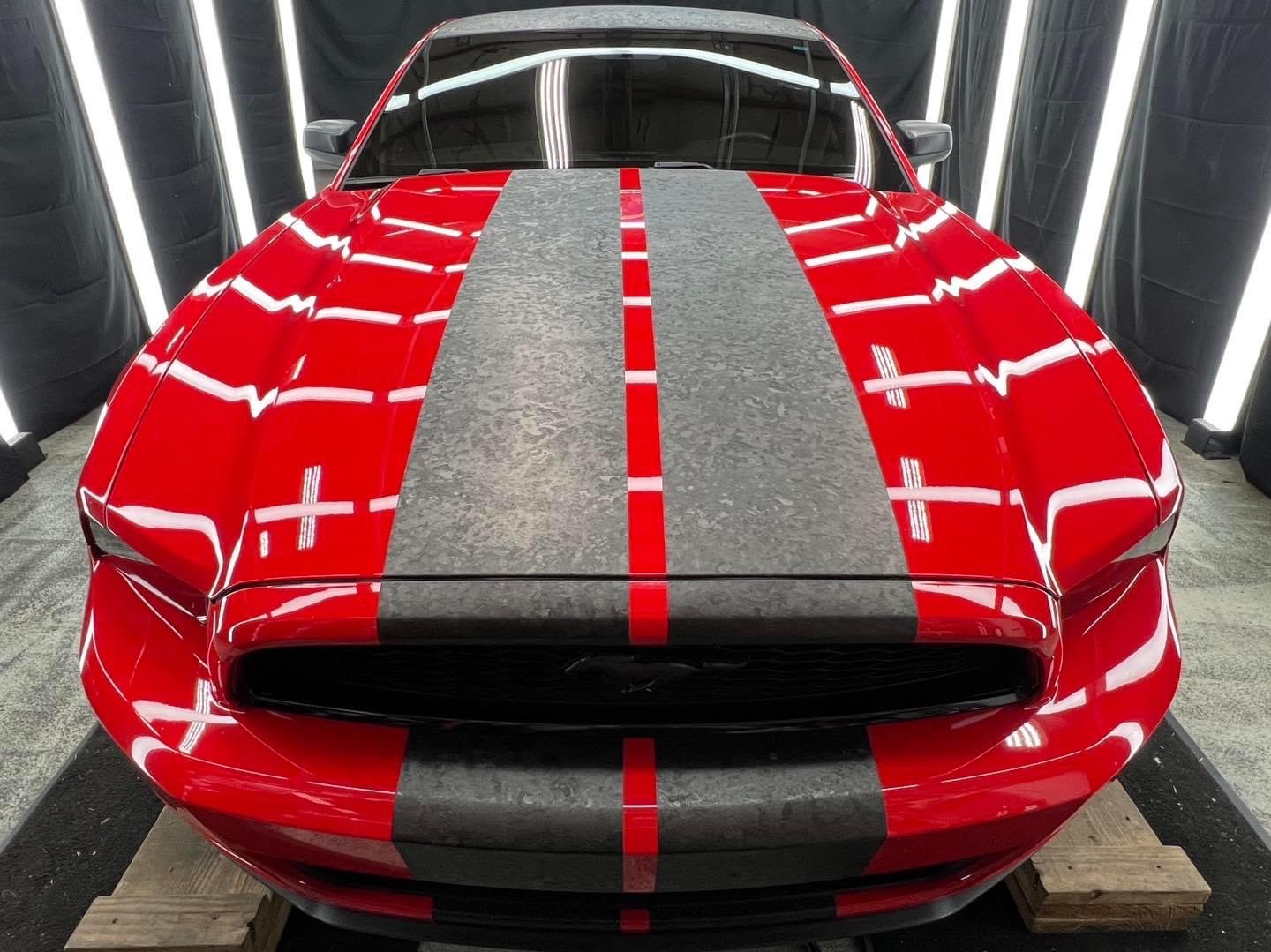 Front view of a red sports car with gray racing stripes.