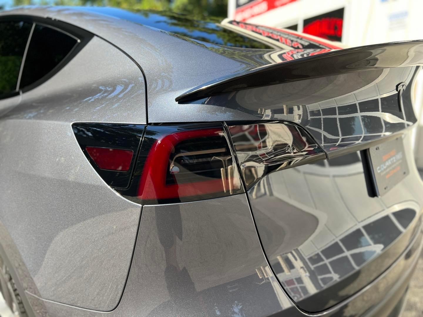Close-up of a gray car's rear with tinted taillights and a carbon fiber spoiler.