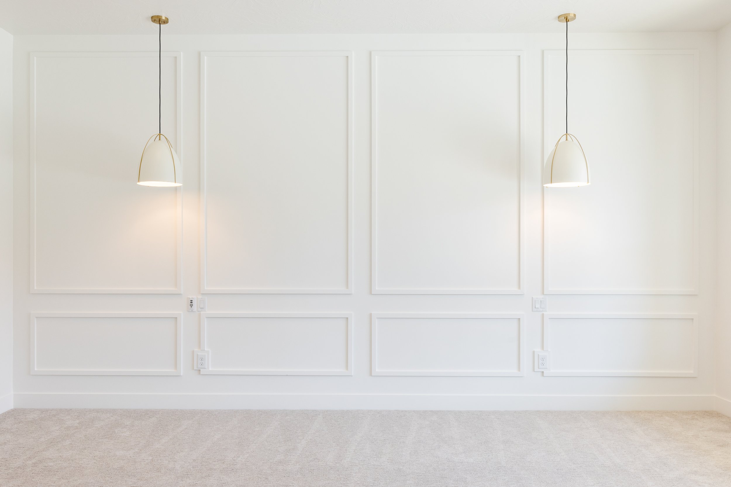 Empty white wall with decorative molding and two hanging pendant lights, beige carpeted floor.