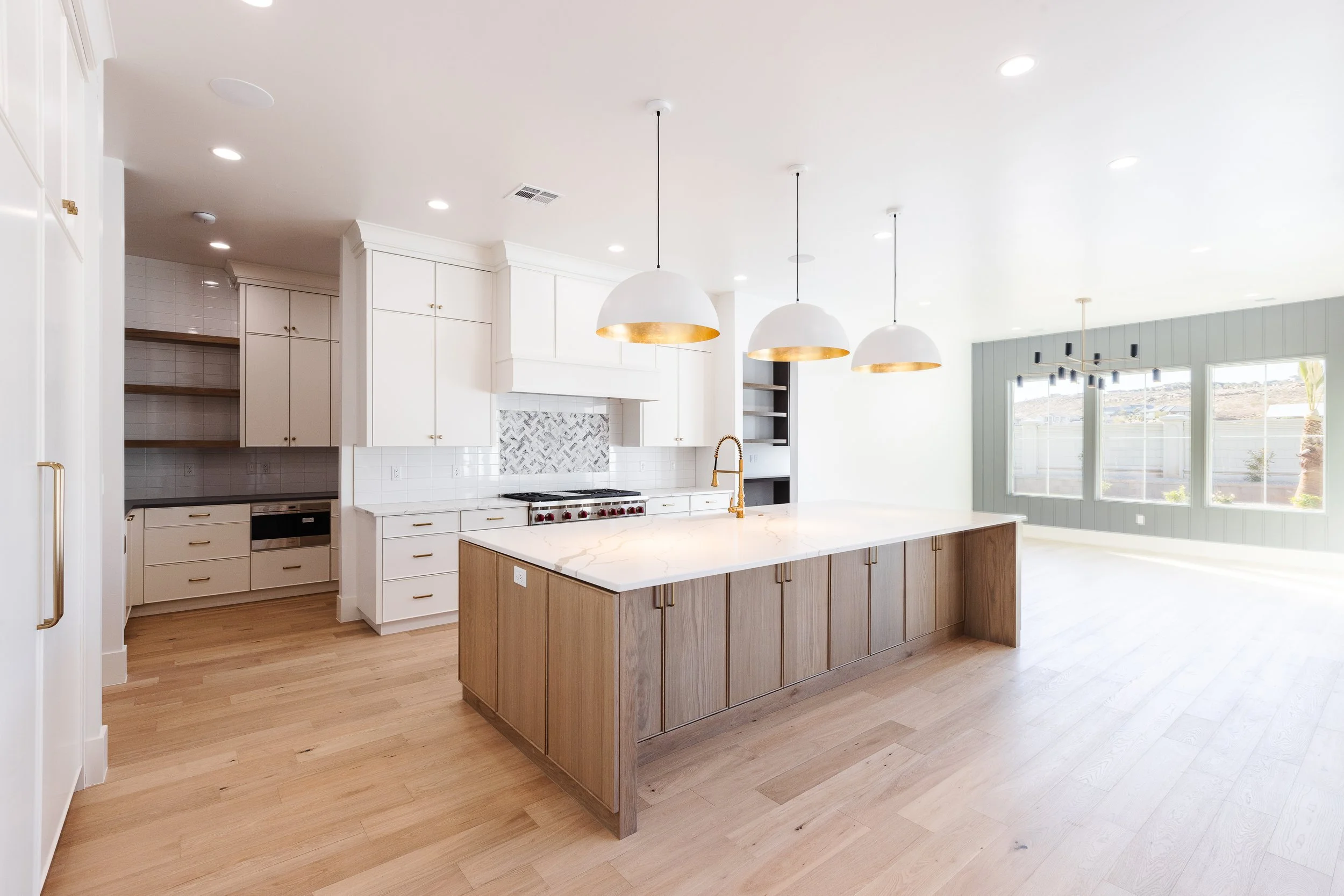 Modern kitchen with white cabinets, wooden island, pendant lights, and large windows.