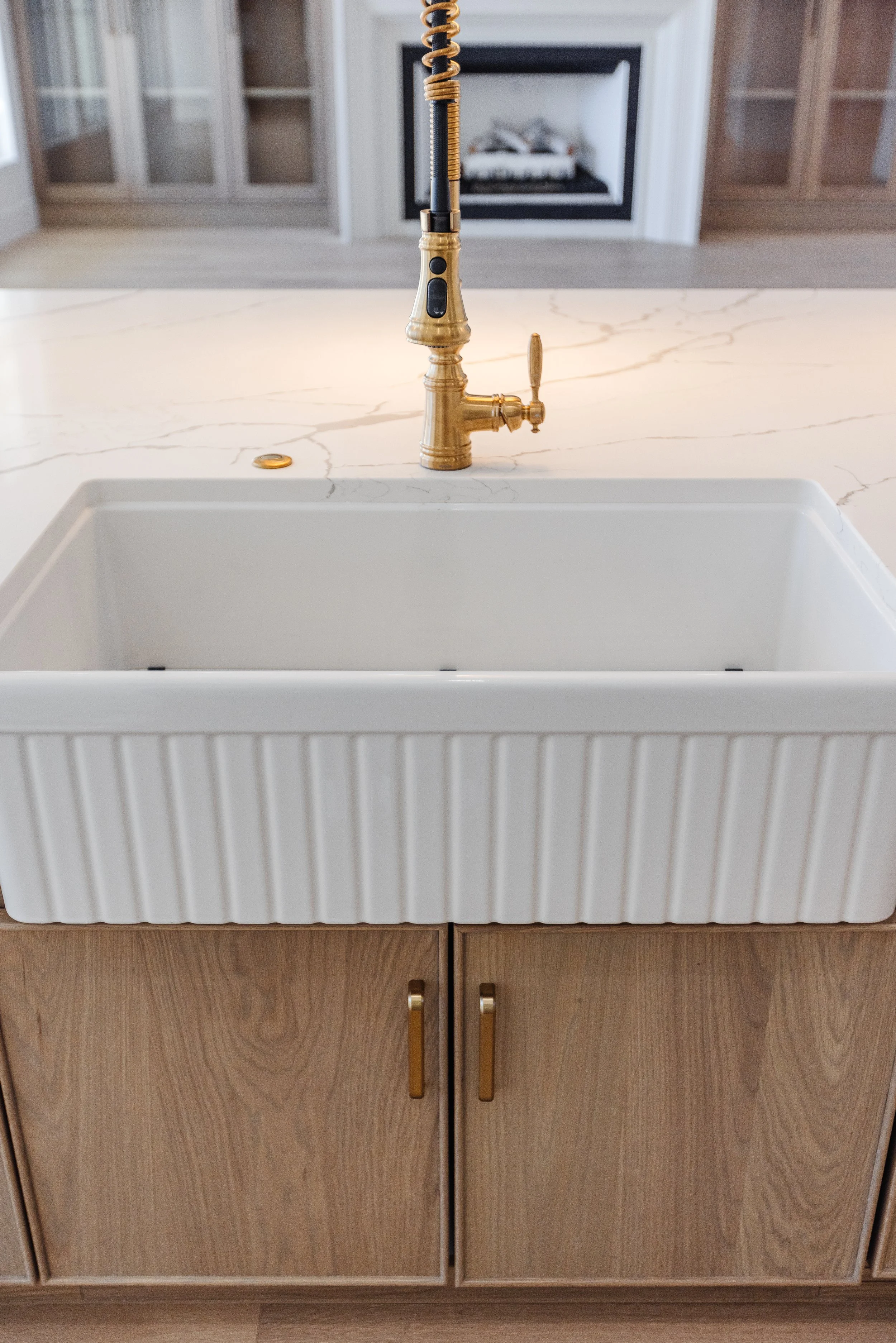 A kitchen island with a white sink, a gold-colored faucet, and cabinet doors below with gold handles.