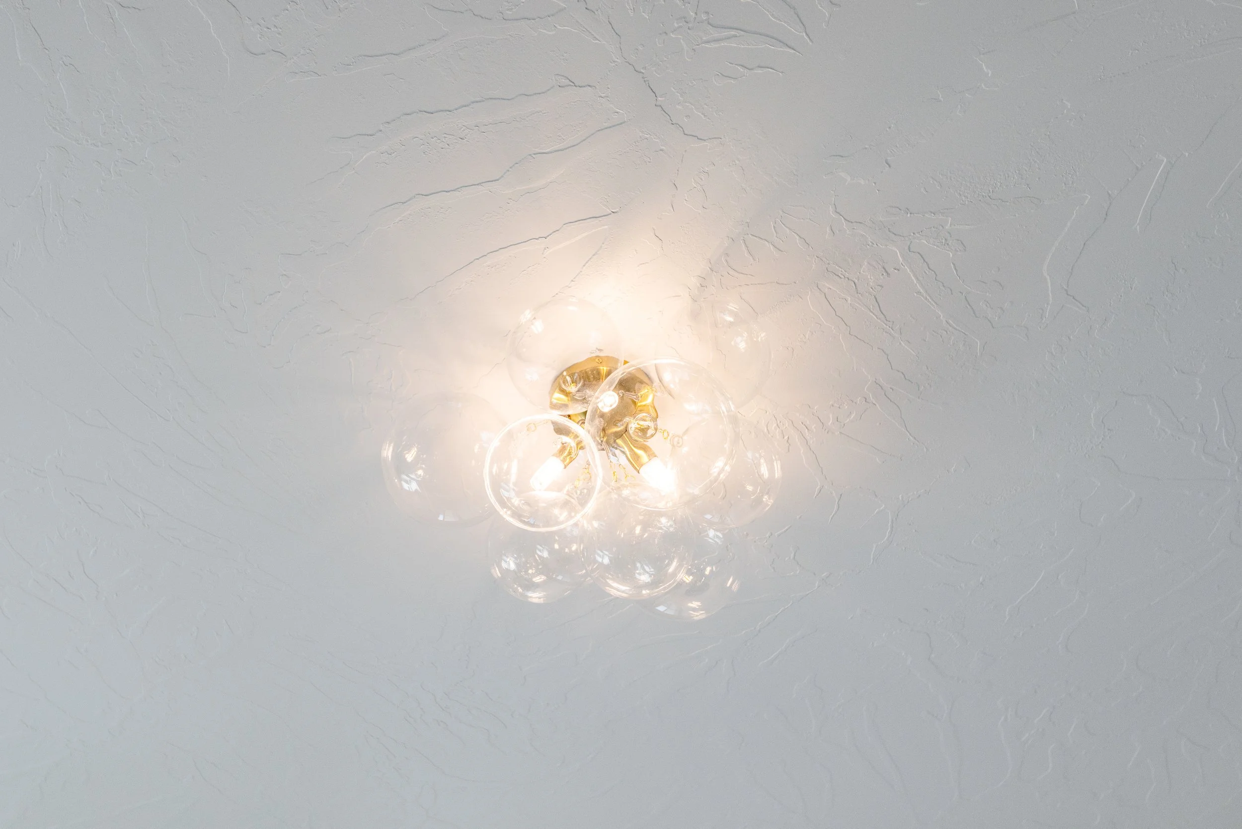 Ceiling light fixture with multiple glass bulbs and gold accents, mounted on a textured white ceiling.