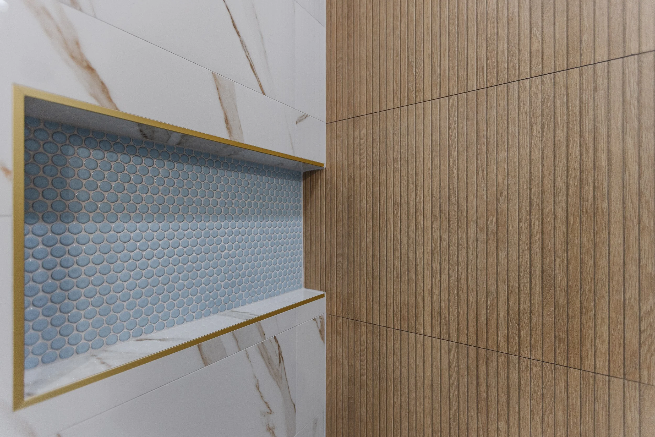 Interior of a modern room with a wooden floor, white marble wall, and a shelf with blue circular tiles.