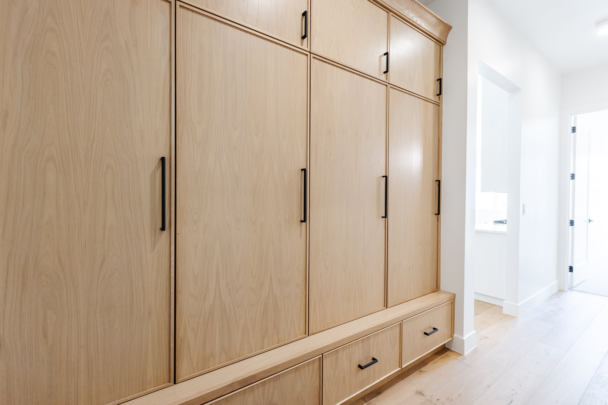 Light wood built-in cabinet with black handles in a bright white room.