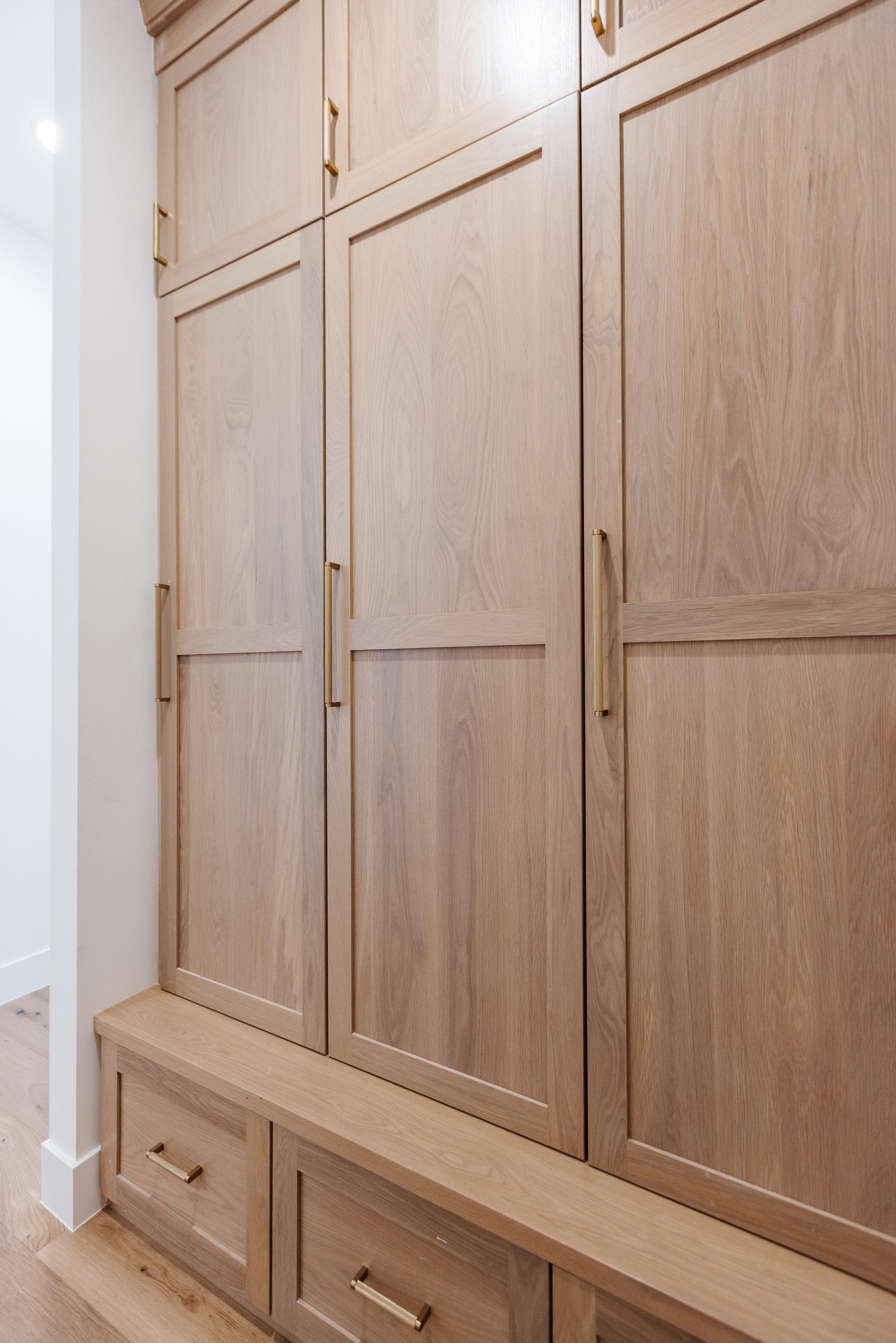 A built-in wooden cabinet with multiple doors and drawers, featuring gold handles, situated against a white wall.