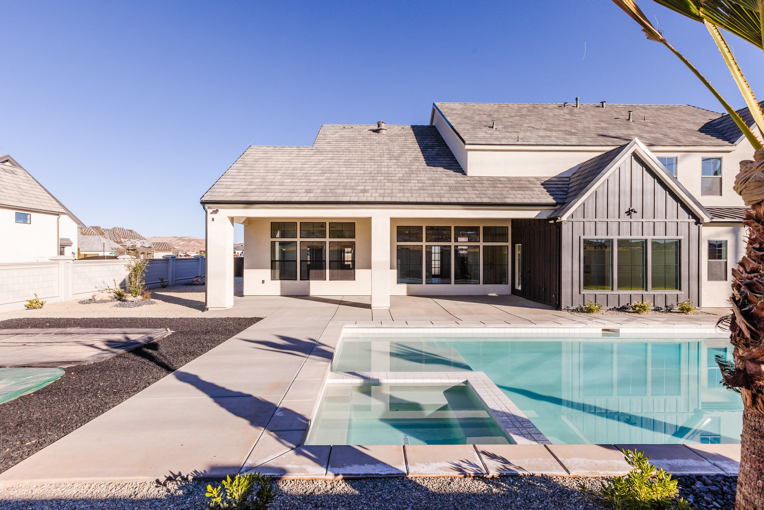 Rear view of modern house with a swimming pool in the backyard, a small landscaped yard, and a clear blue sky.