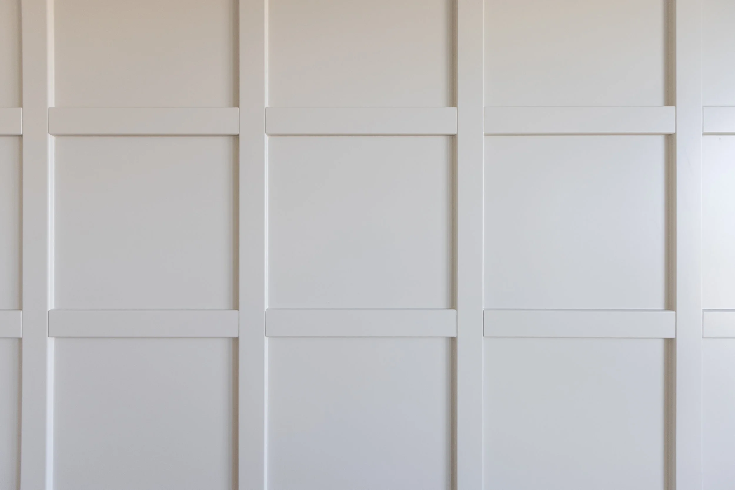 Close-up of a white, paneled garage or wardrobe door with a grid pattern created by the panels and frames.