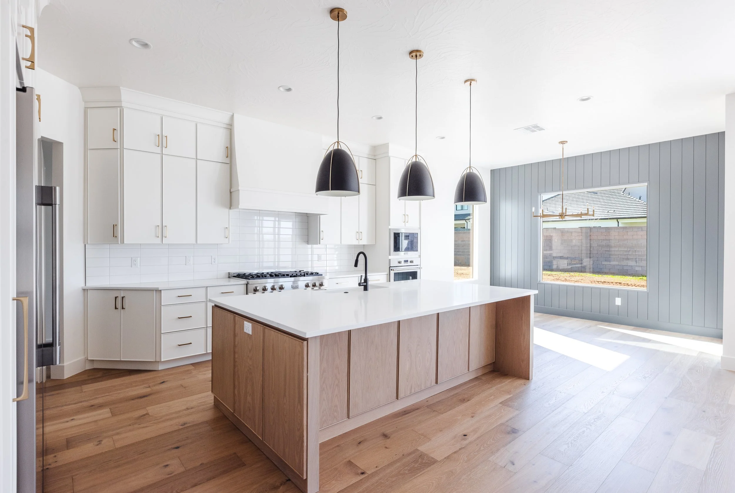 Modern kitchen with white cabinets, black pendant lights, a wooden island, large window, and wood flooring.