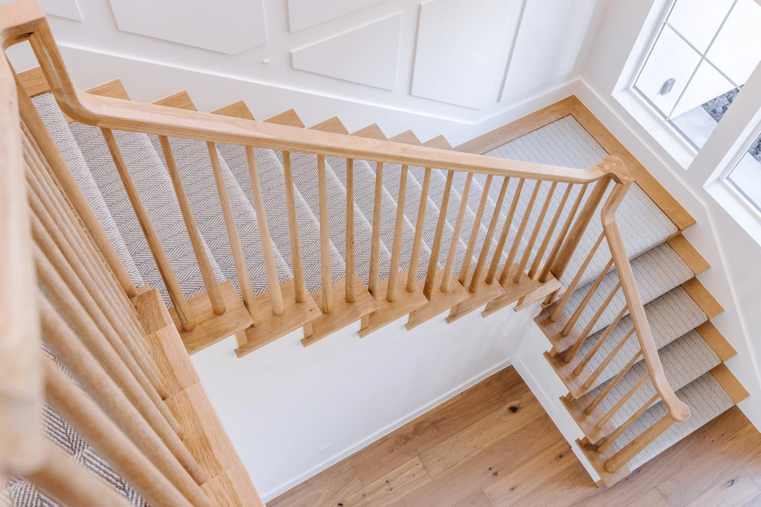 View of a staircase with light wood handrail, carpeted steps, and a large window letting in natural light.
