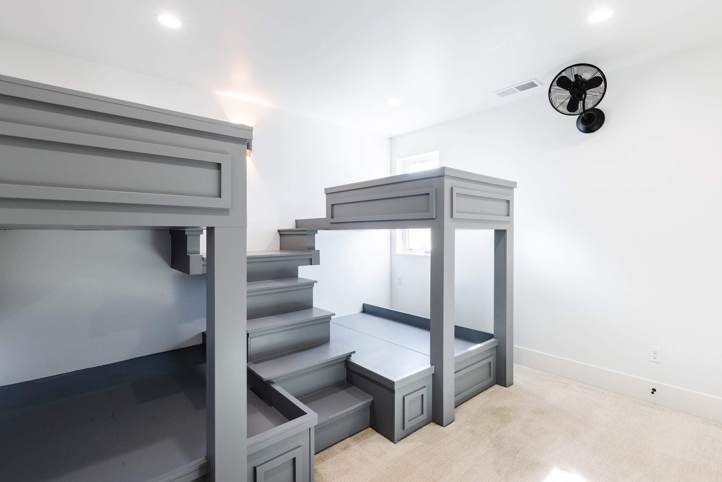 Interior of a room with gray custom-built bunk beds with stairs, a ceiling fan, and white walls.