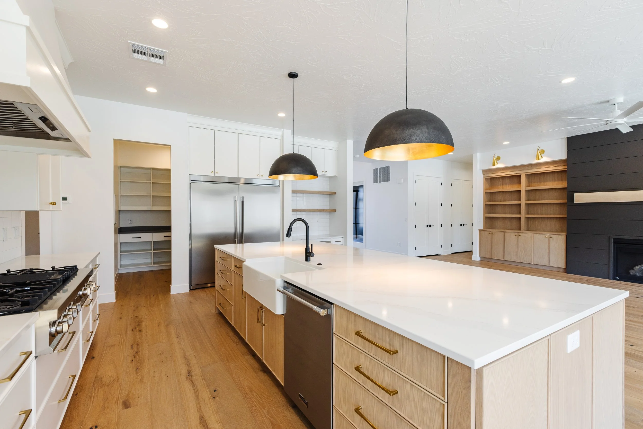 Modern kitchen with white cabinets, a large island with a white countertop, black and gold pendants, stainless steel appliances, and hardwood floors.