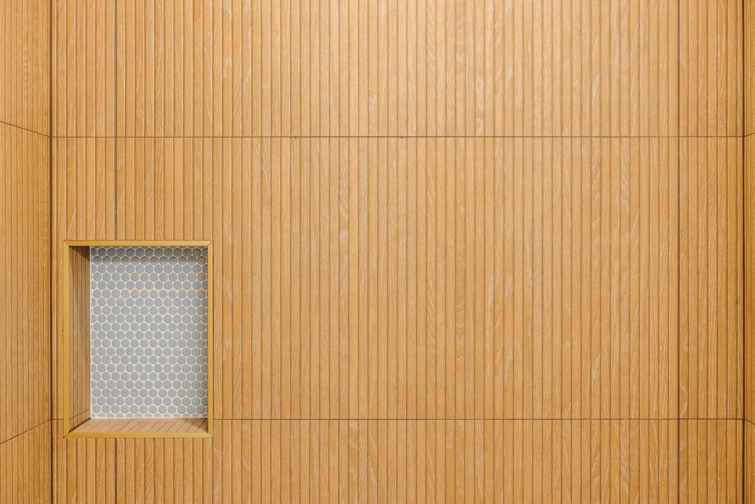 A wall with vertical wooden panels and a small rectangular ventilation opening with a honeycomb mesh.