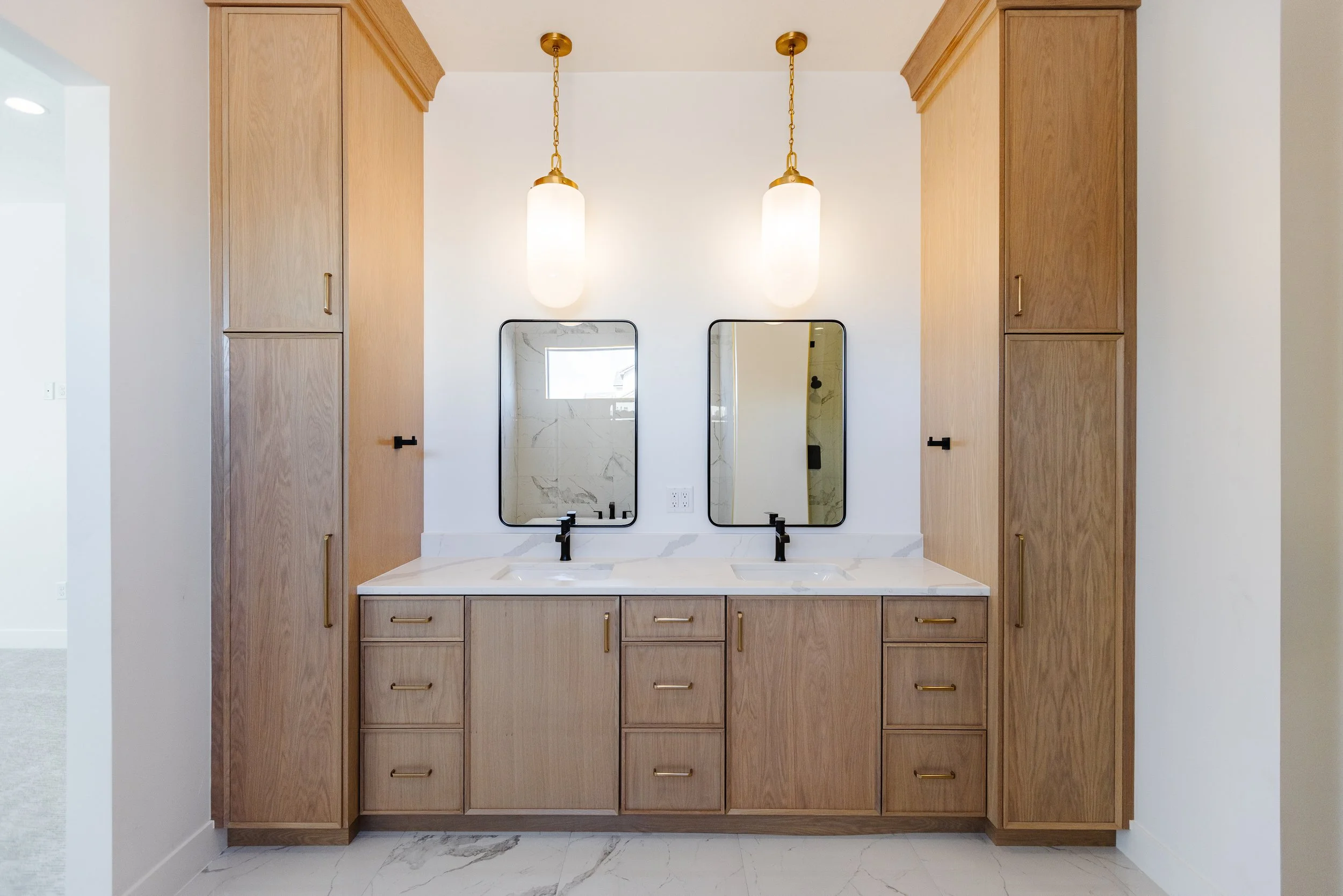 Bathroom vanity with wooden cabinets, twin mirrors, black faucets, and hanging pendant lights.