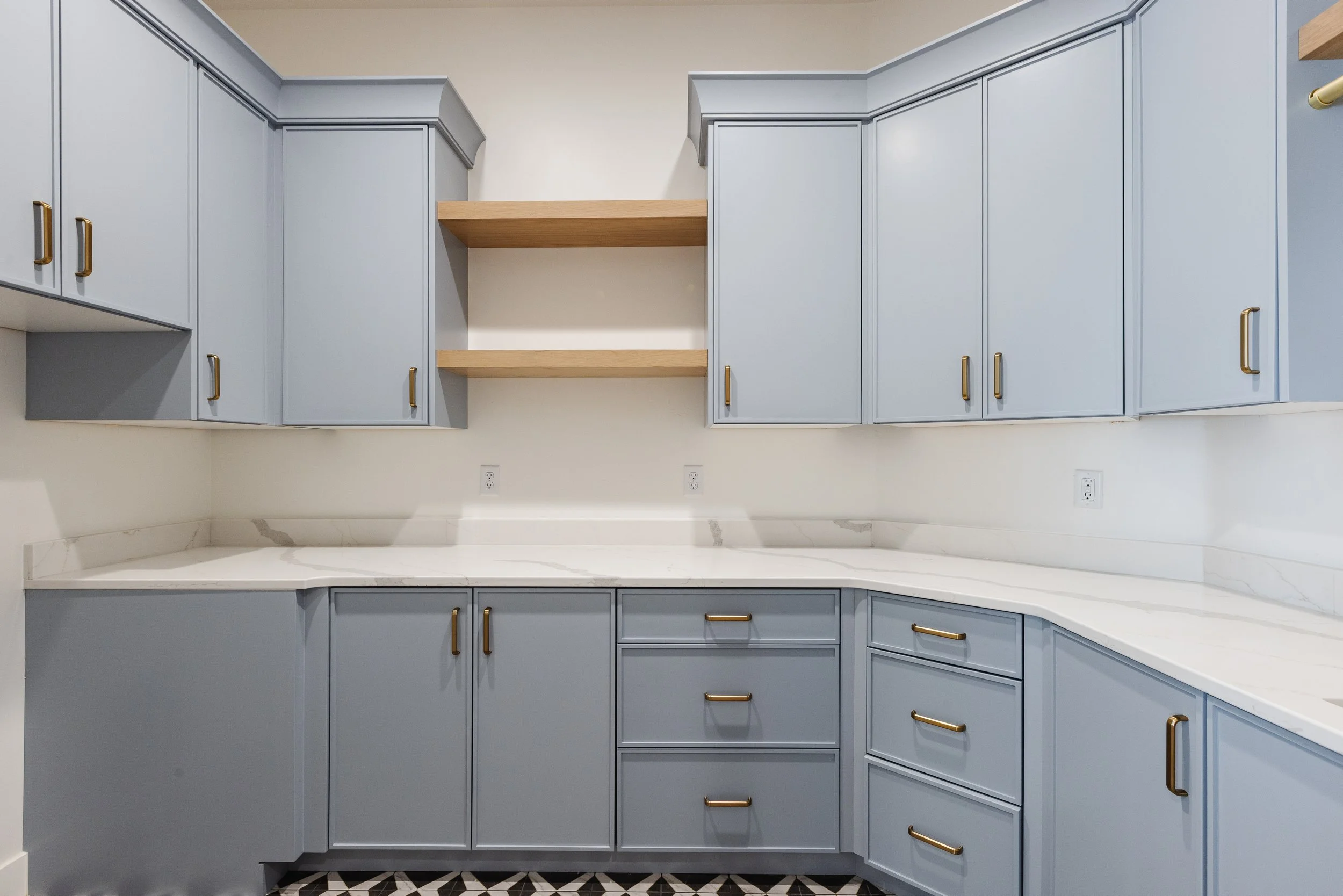 Kitchen with blue cabinets, gold handles, white marble countertop, and open wooden shelves between cabinets.