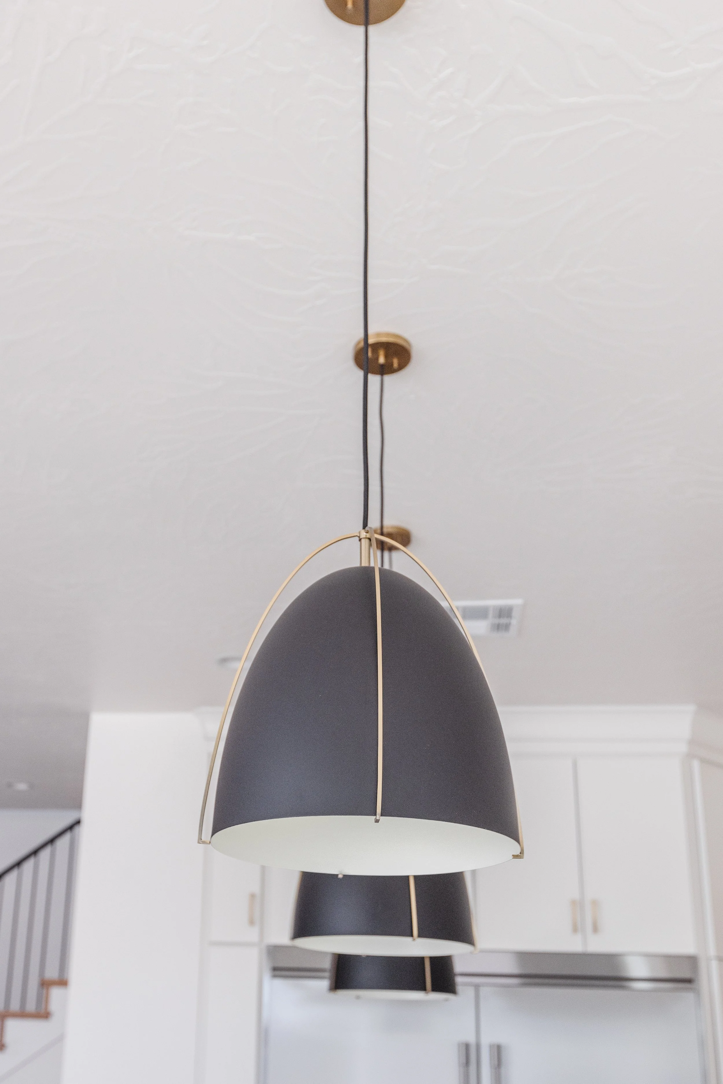Close-up of a modern pendant light with a black shade and gold accents hanging from a ceiling with textured white paint.
