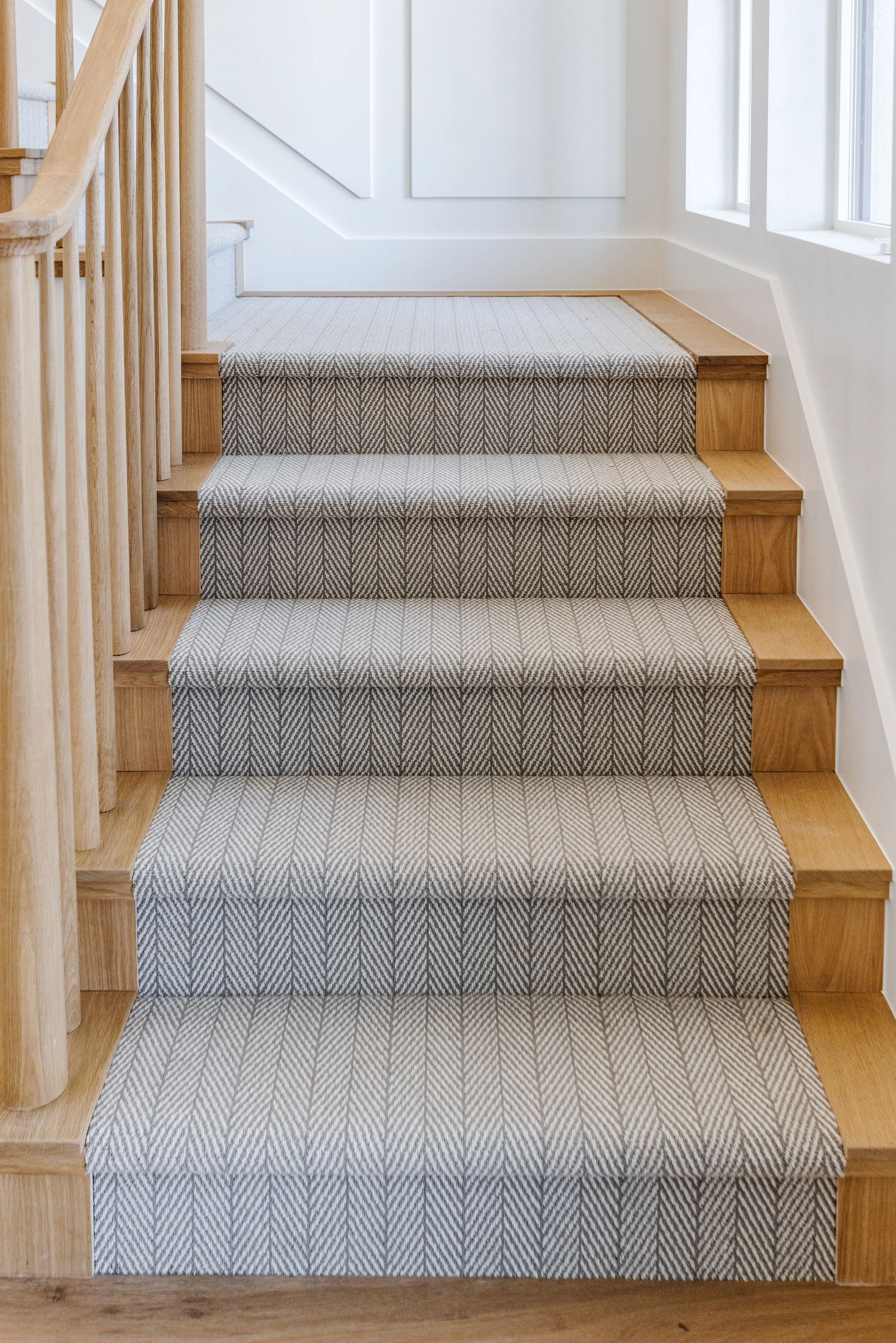 Interior view of a staircase with wooden railings and carpeted steps in a home, near a window.