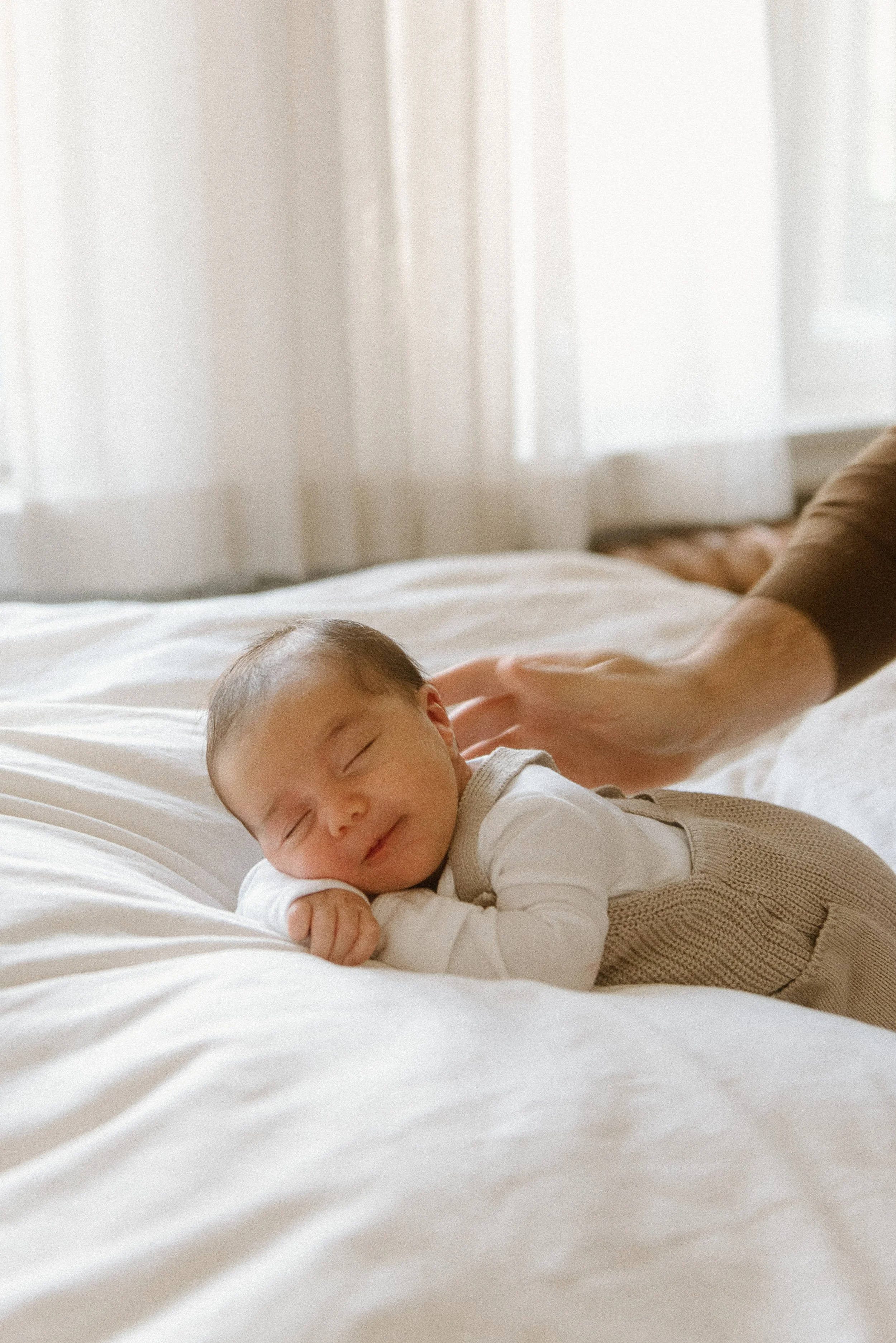 Newborn sleeping peacefully with father's hand nearby.