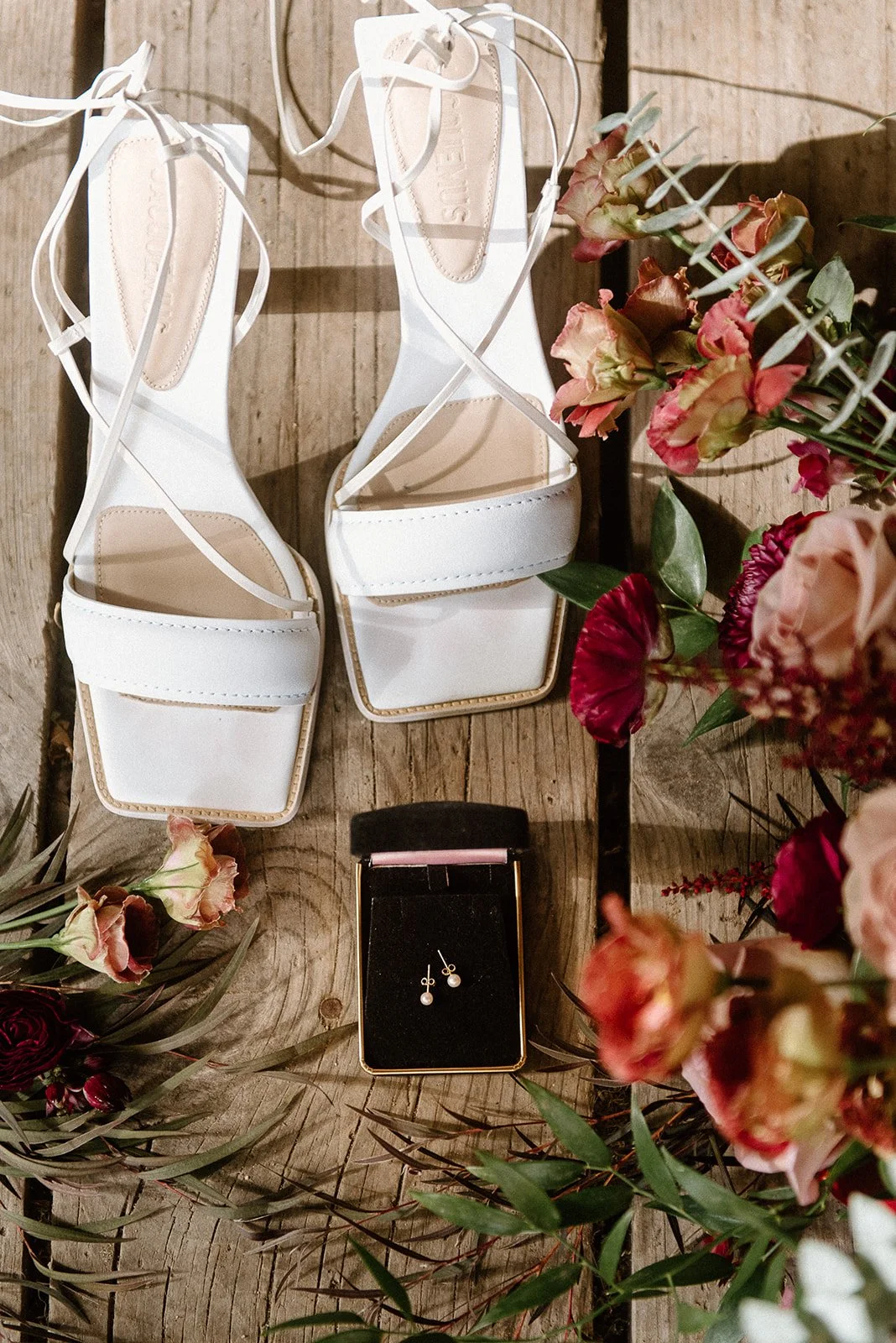 White shoes on a wooden deck with earings and flowers