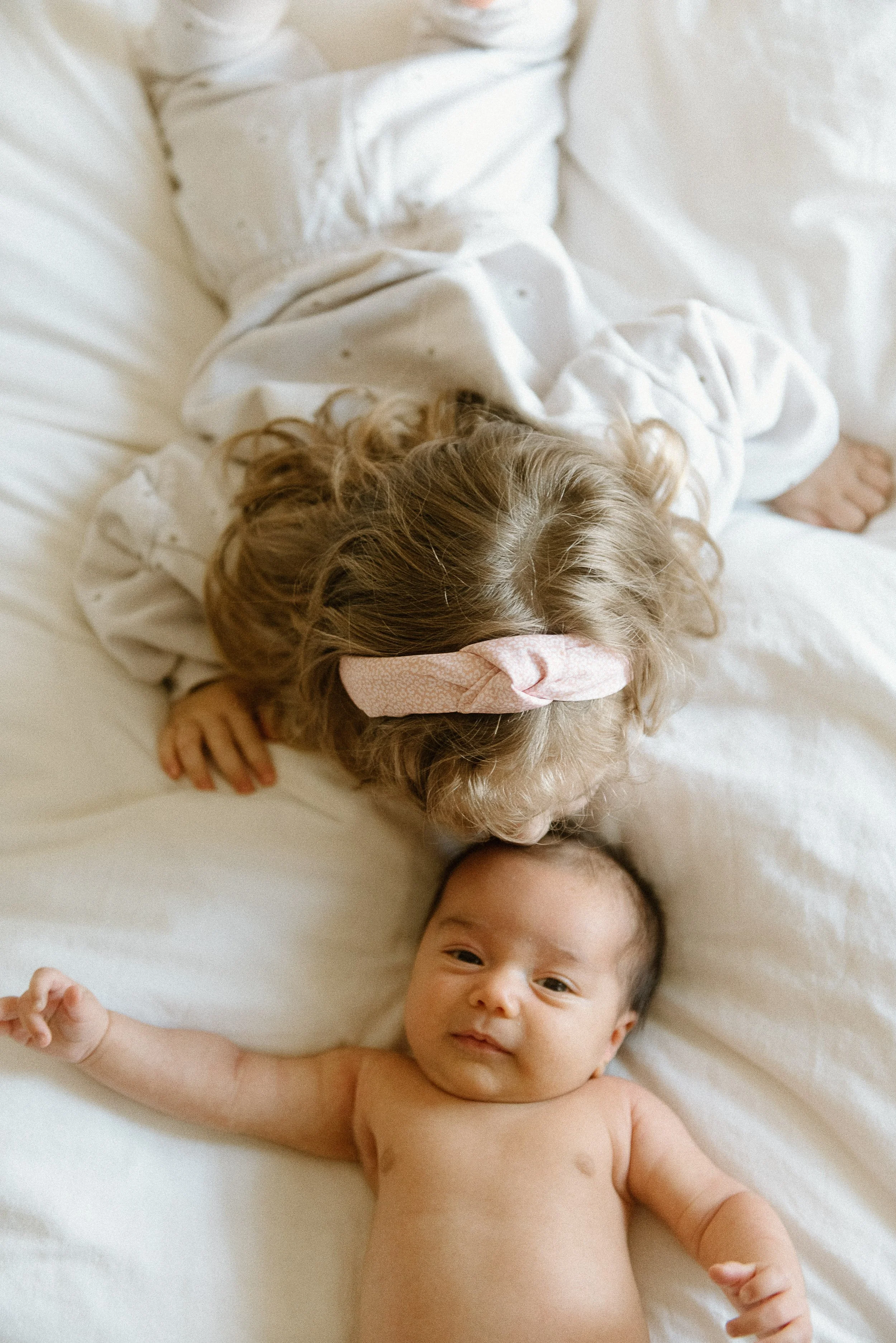 Sister kisses newborn brother on bed.