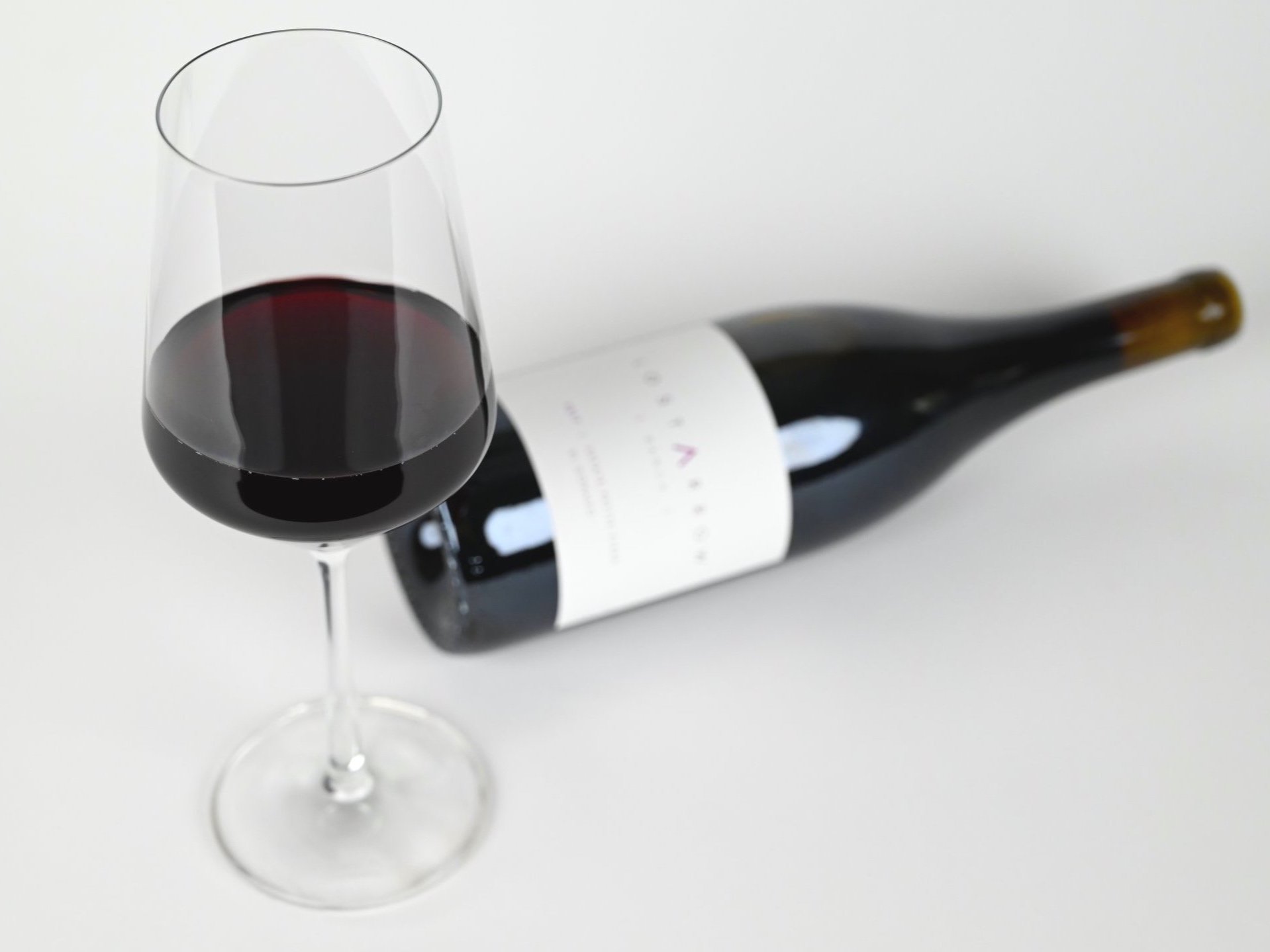 A photograph of a glass of red wine in front of a reclining bottle of Petite Sirah.