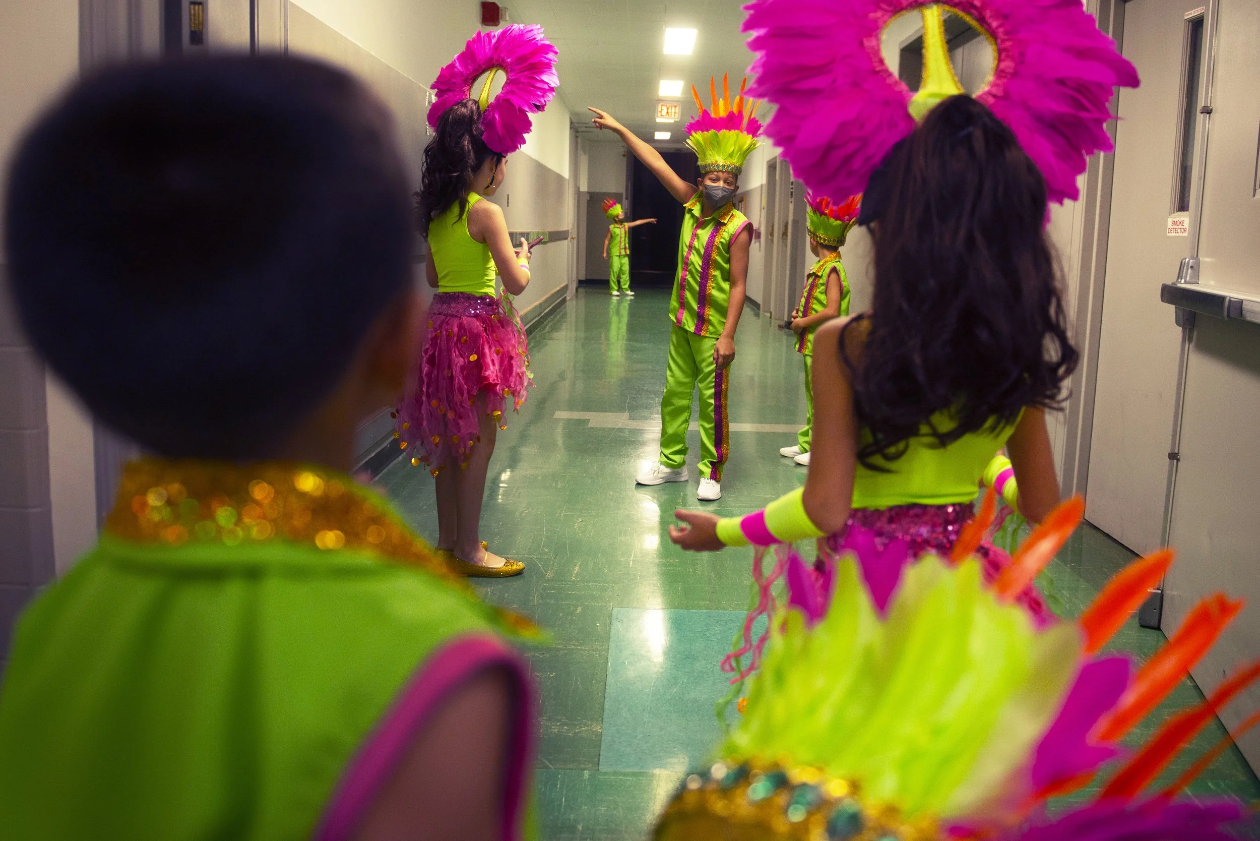 Children, anxious to start the show soon, point down towards the stage doors from the changing rooms. They have been preparing their costumes, applying makeup and going over their musical dance performance with their choreographer for two hours and h