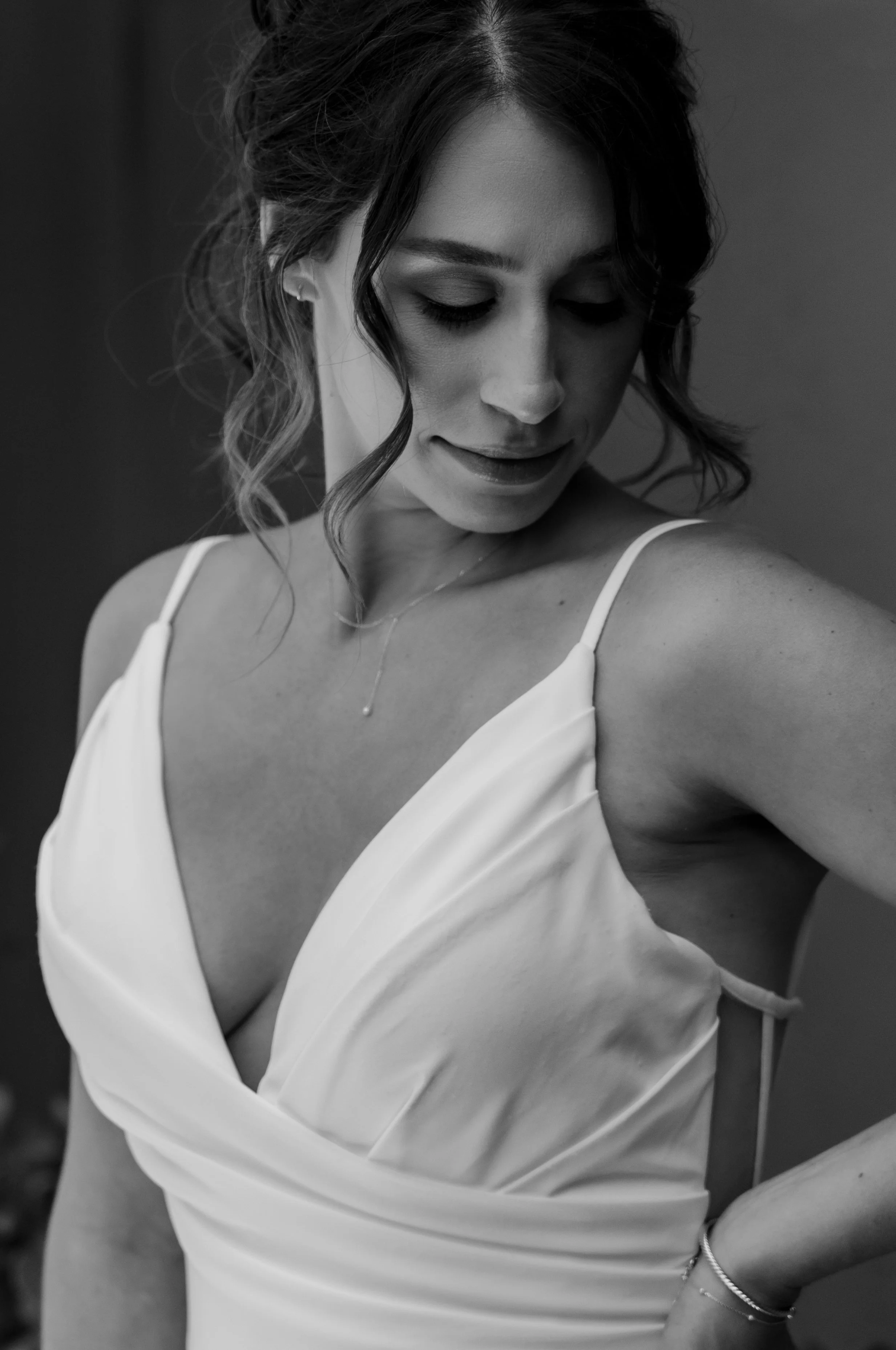 Wedding photographers in Southern California. A woman wearing a white dress with spaghetti straps, looking down and smiling softly.