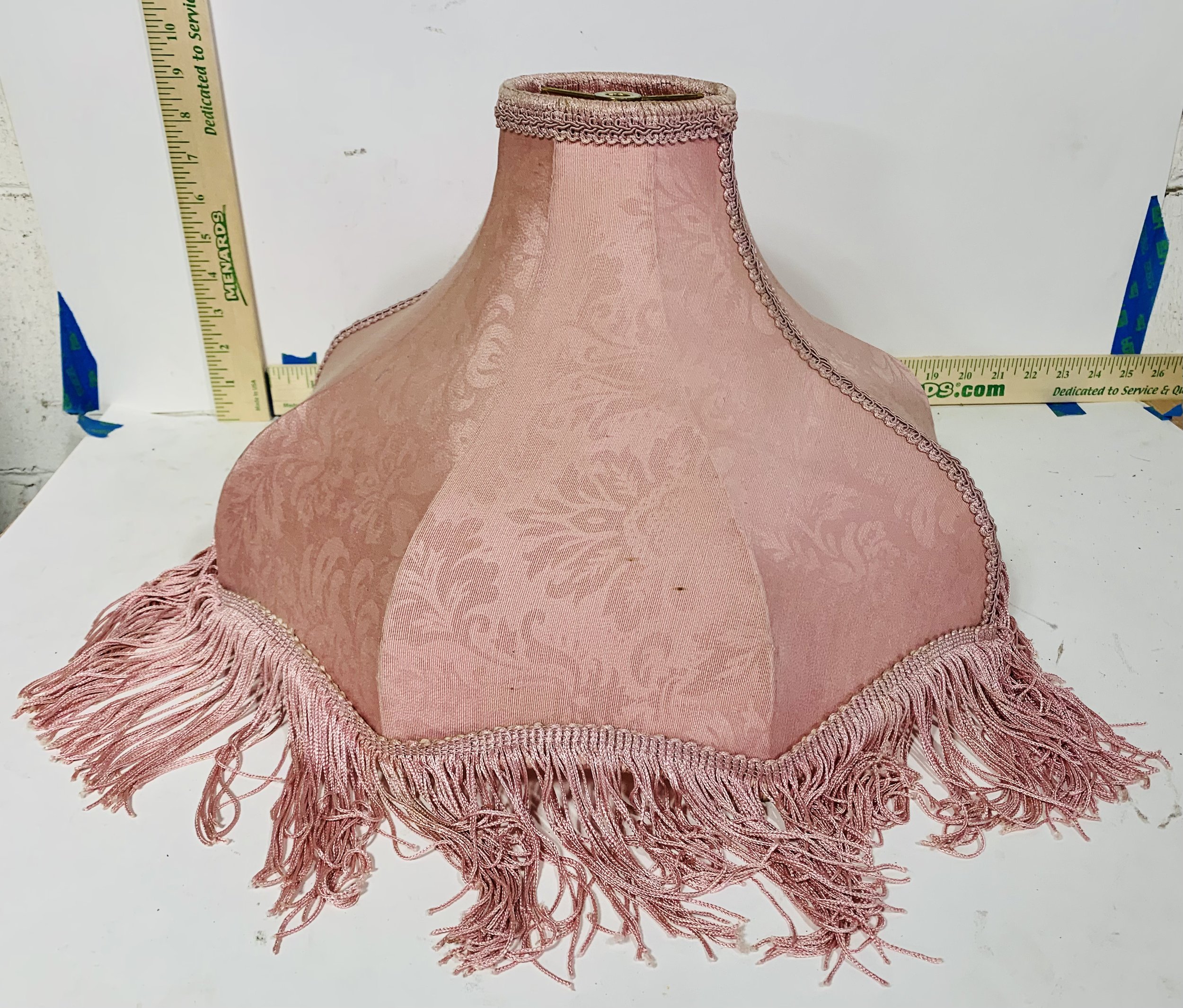 Pink fringed lampshade on white background with rulers