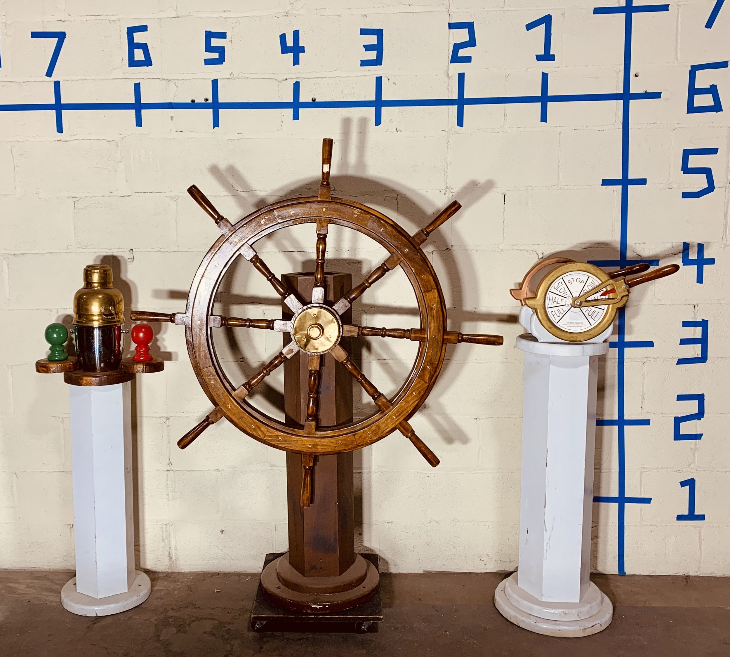 Wood captains wheel and other ship instruments against white wall with dimensions