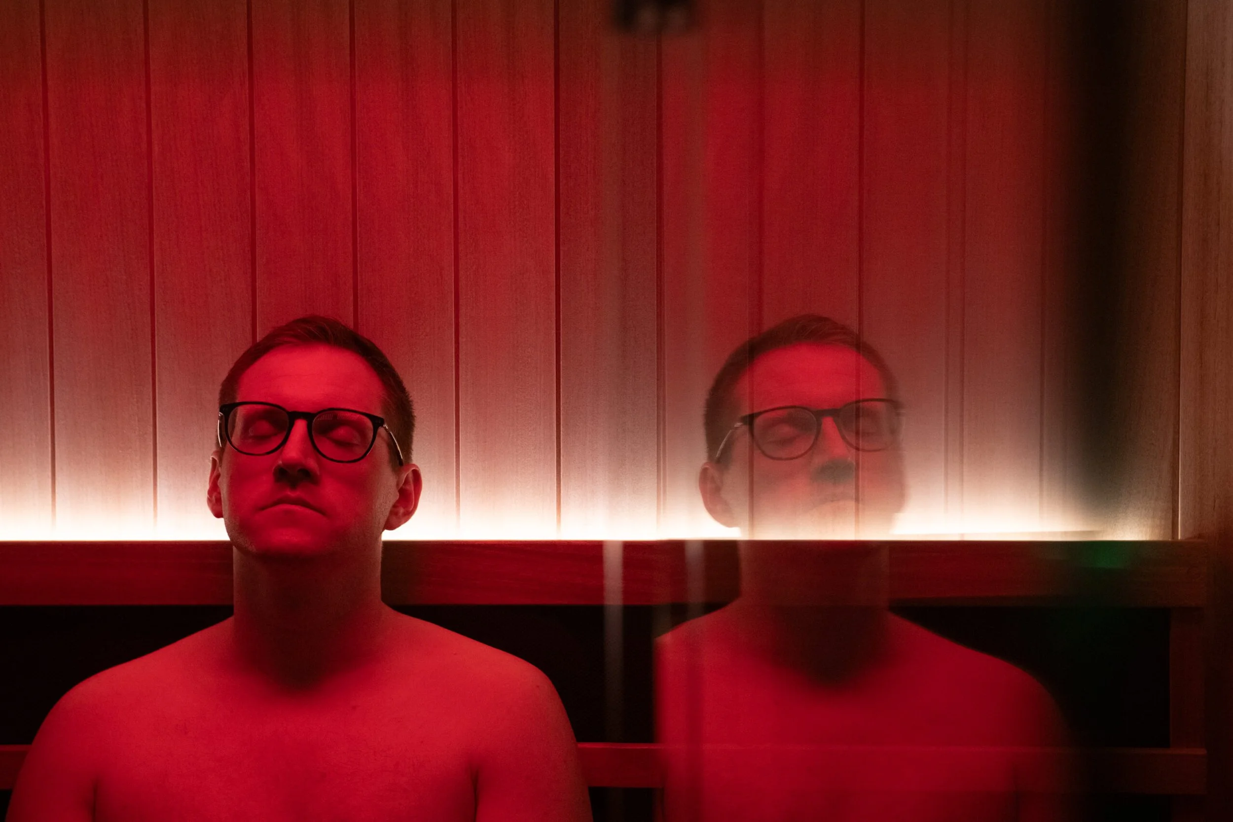 Guest seated in the private infrared sauna at Being Wellness Centre in St Albans, surrounded by warm timber finishes and relaxing ambient lighting during a wellness session.