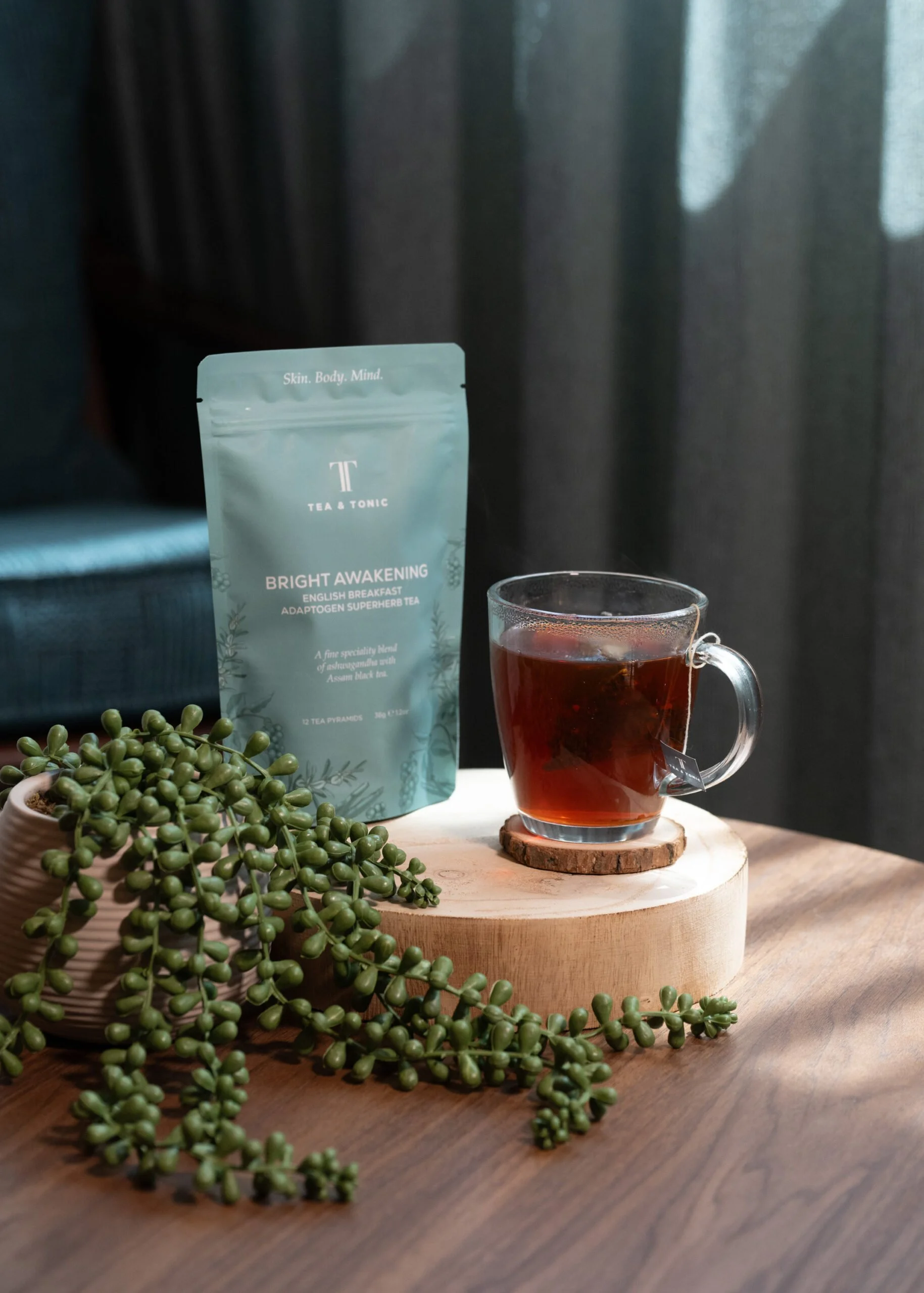 A glass cup of Tea & Tonic Bright Awakening herbal tea on a wooden table at Being Wellness Centre in St Albans, served as part of a relaxing wellness experience.