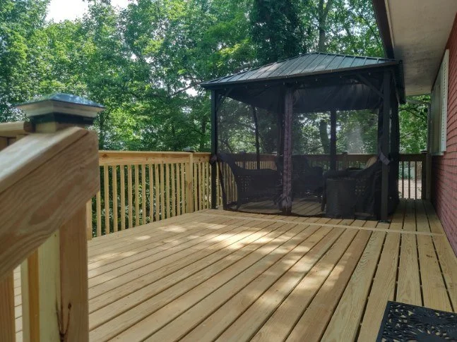 Newly constructed wooden deck with a black screened outdoor gazebo and lush green trees in the background.