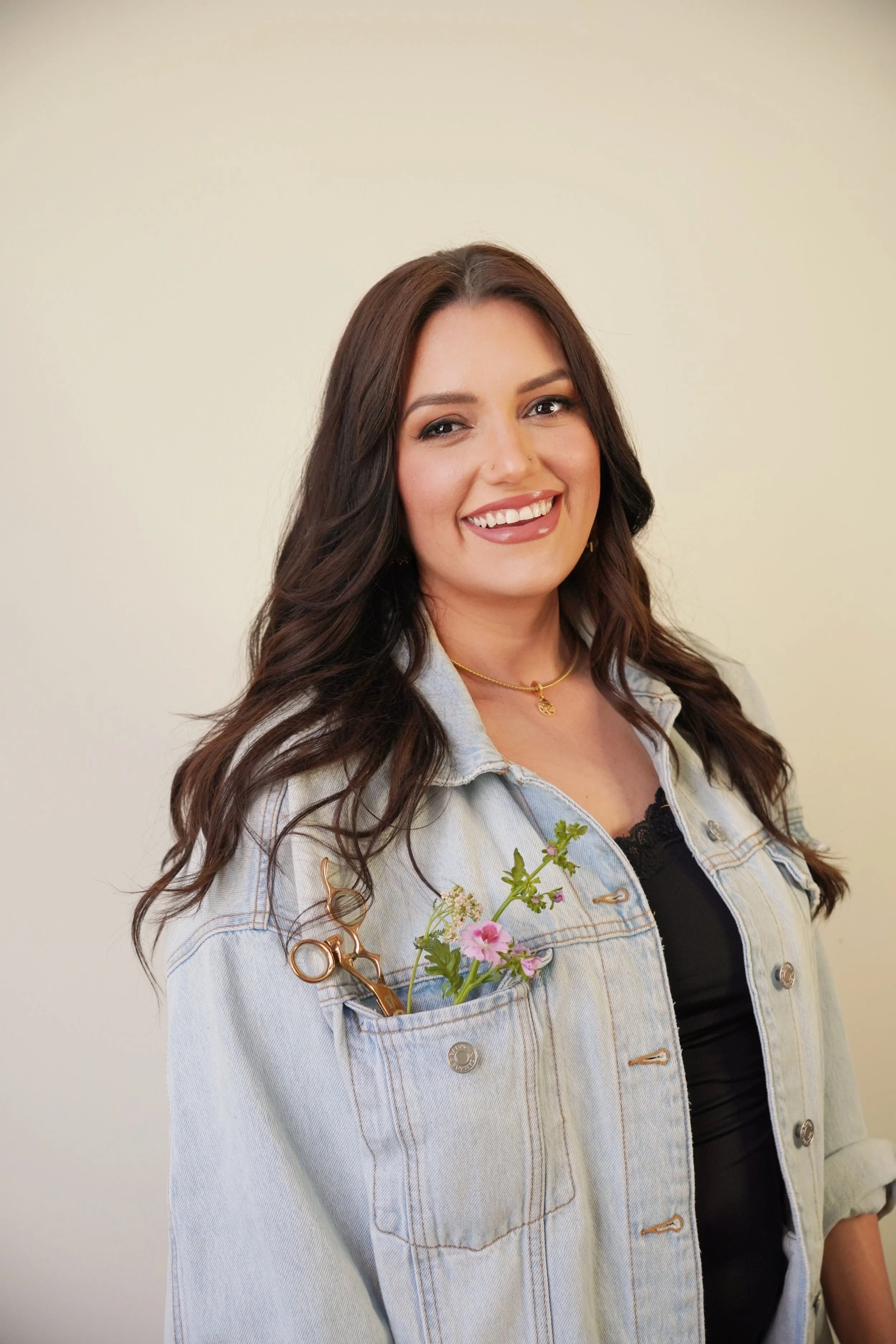 Brunette hair stylist smiling with flowers and hair cutting shears in her pocket