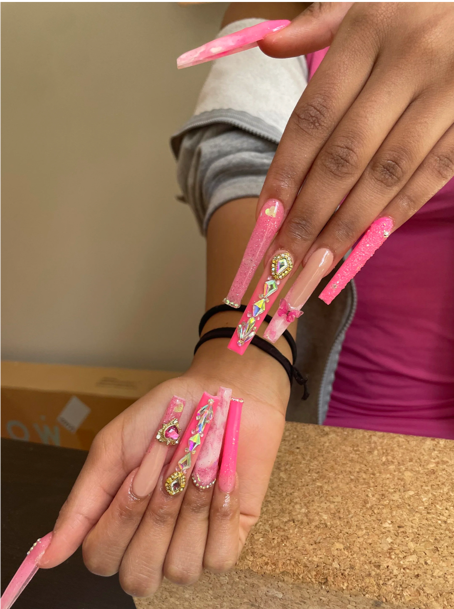 a photo of pink acrylic nails, extra long with gold and crystal accents