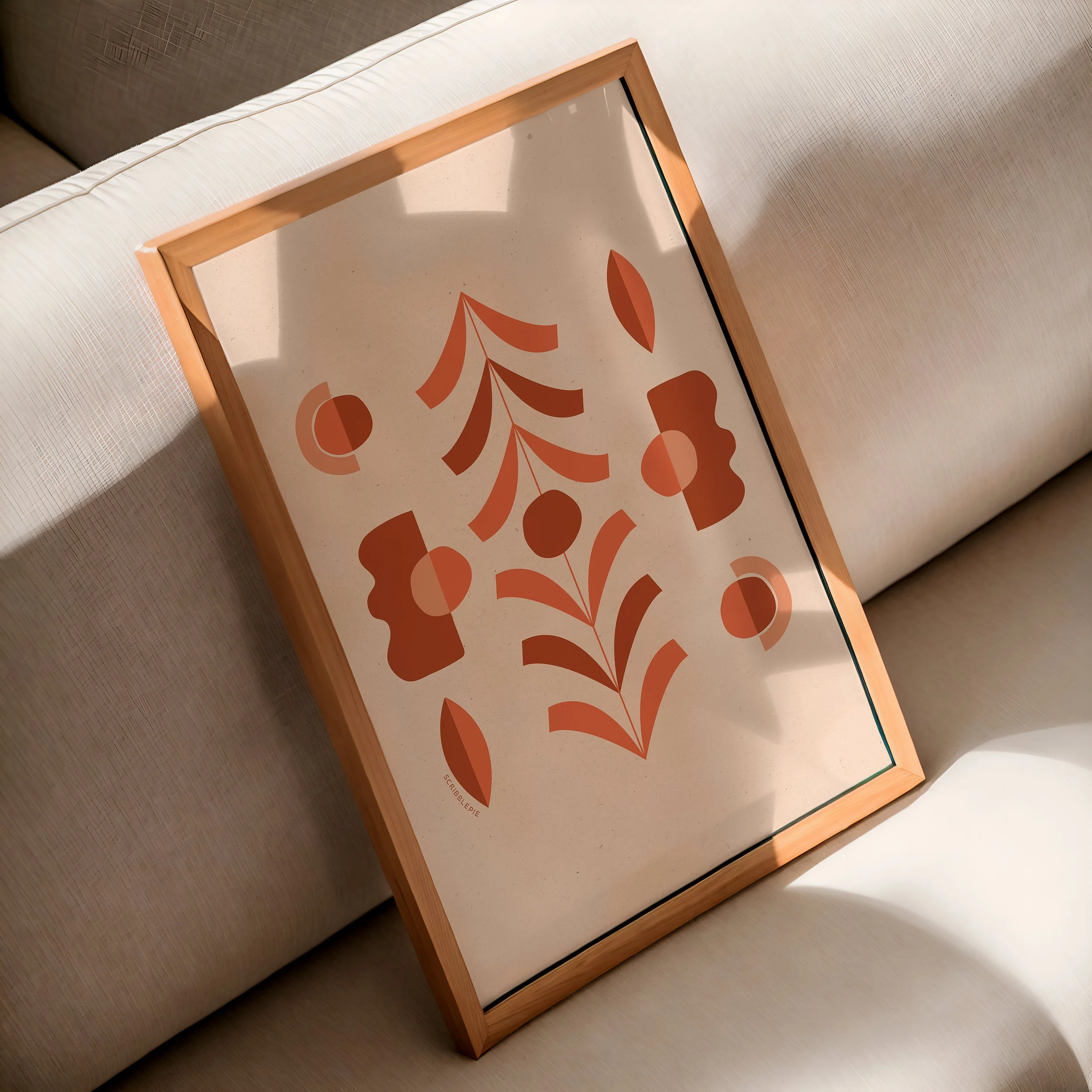 Photo of a framed picture lying on a beige couch with textured fabric. The picture features a stylized orange leaf design.