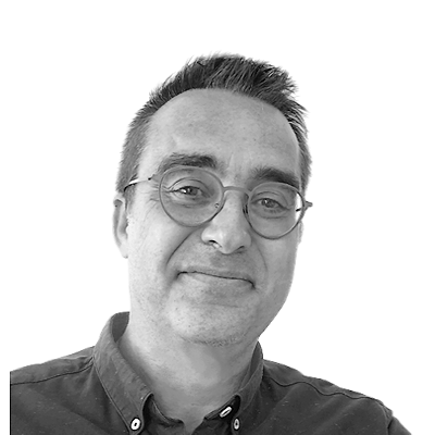 Portrait d'une personne portant des lunettes et une chemise, en noir et blanc.